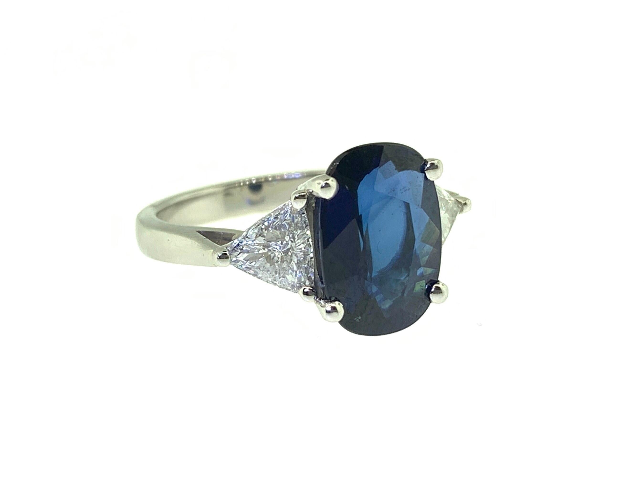 This beautiful cocktail ring showcases a stunning GIA Certified 4.01 carat Cushion Sapphire flanked by two Trillion Cut Diamonds (0.85 carats) set in Platinum. Ring size is 6.