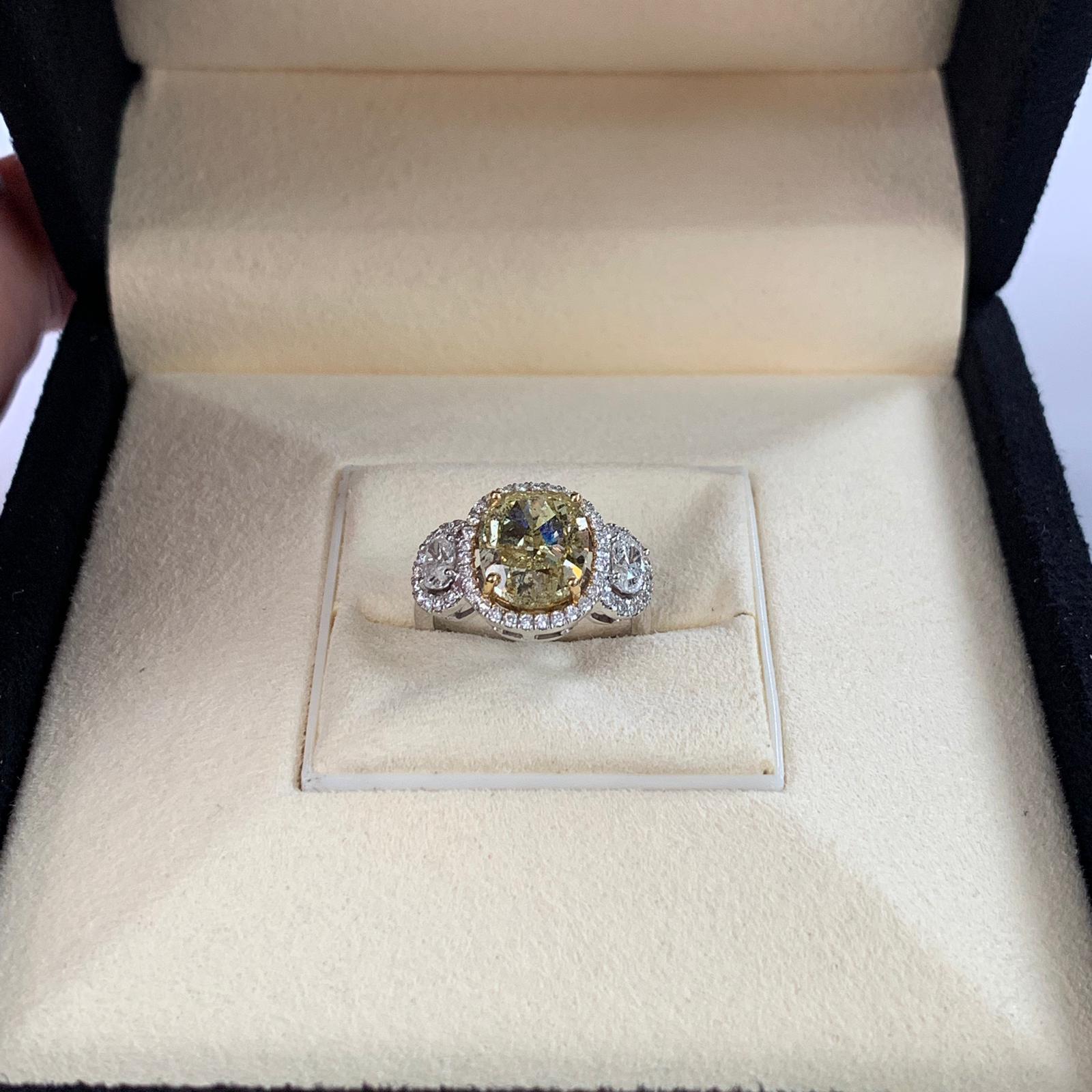 Natural fancy yellow cushion cut diamond weighing 4.01 carats. Certified by GIA. beautifully accompany by 2 oval diamonds and set in 4 prong halo setting. Its transparency and luster are excellent. 18 Karat white gold. this fancy yellow cushion