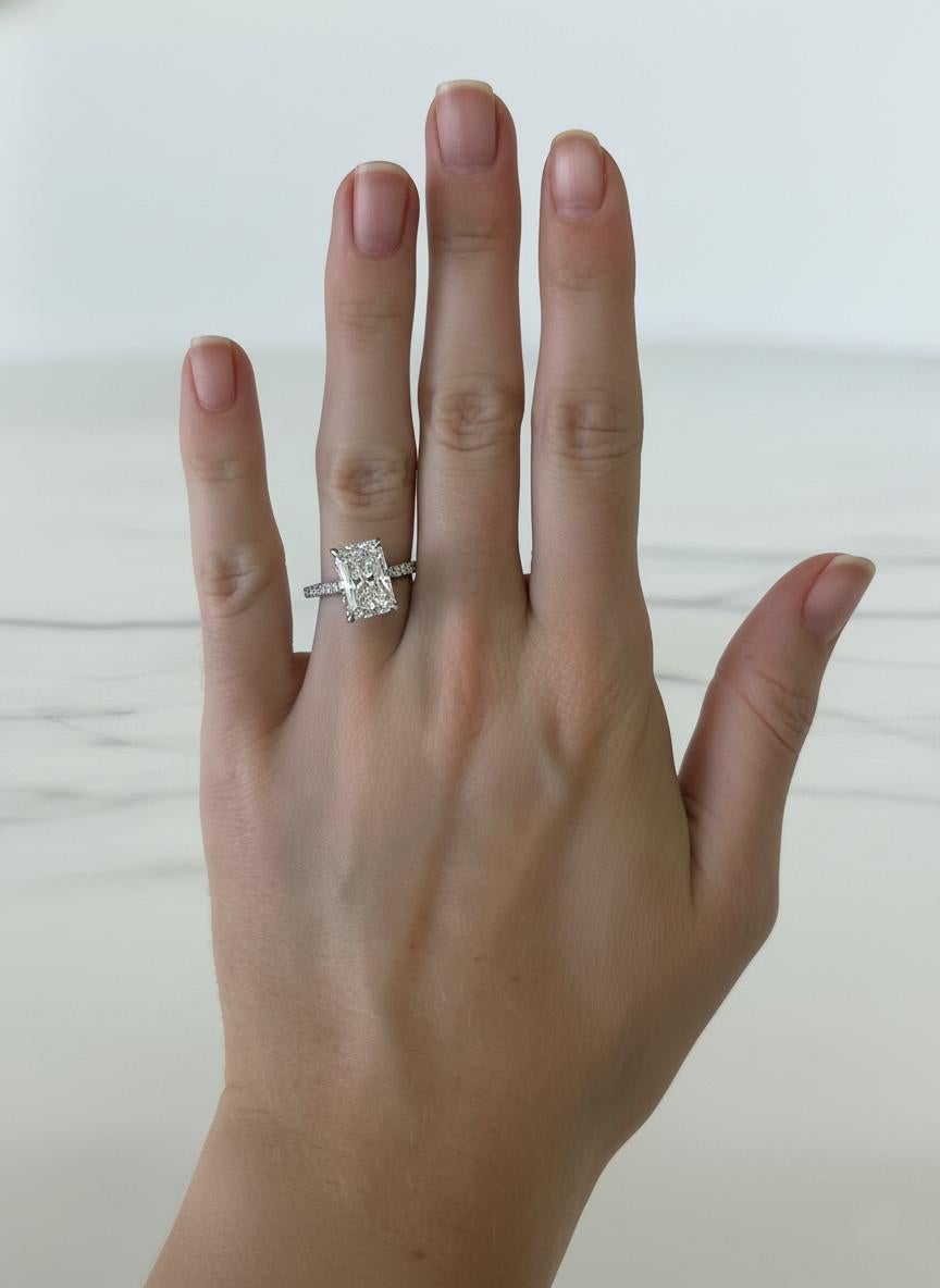 Un spectaculaire diamant de 4 carats de taille radieuse occupe le devant de la scène dans cette bague de fiançailles intemporelle et raffinée. Certifié par le GIA, le diamant présente un bel équilibre de brillance et de feu, avec un grade de couleur