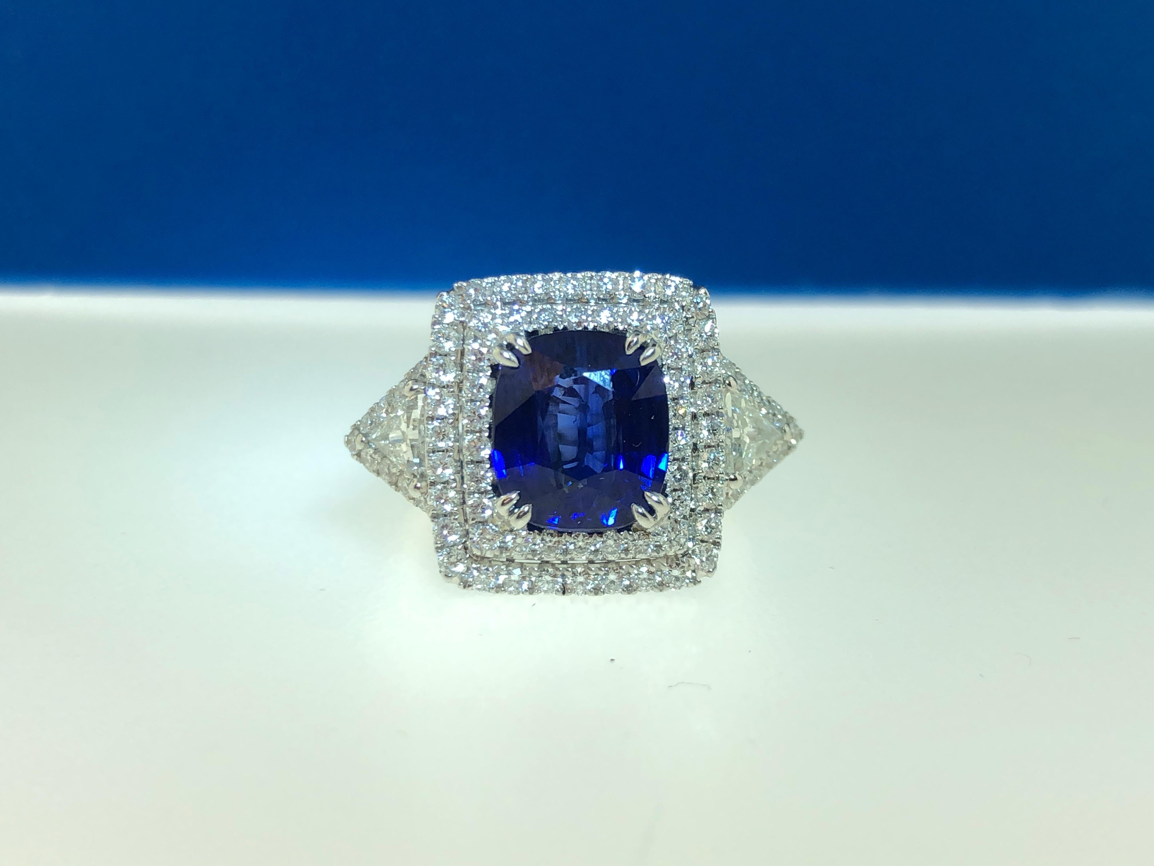 This stunning cocktail ring features a GIA Certified 4.04 carat beautiful blue cushion sapphire with a double diamond halo. The sapphire is flanked by trillion cut diamond side stones, each with its own diamond halo. Total diamond weight = 1.39