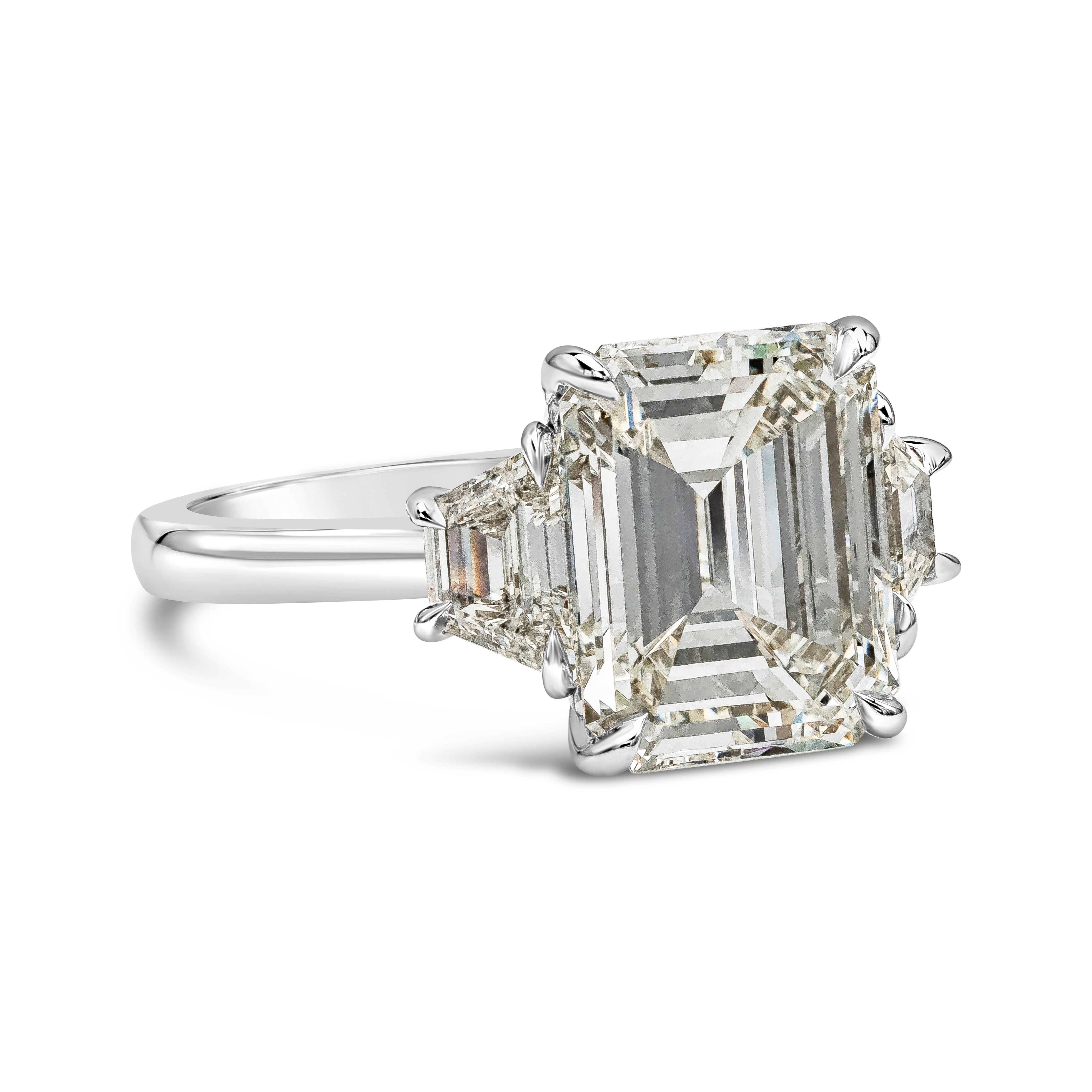 A classic and timeless three-stone engagement ring style showcasing a 4.05 carat emerald cut diamond certified by GIA as K color, VVS2 clarity, flanked by step-cut trapezoid diamonds on either side. Accent diamonds weigh 0.79 carats total. Made in