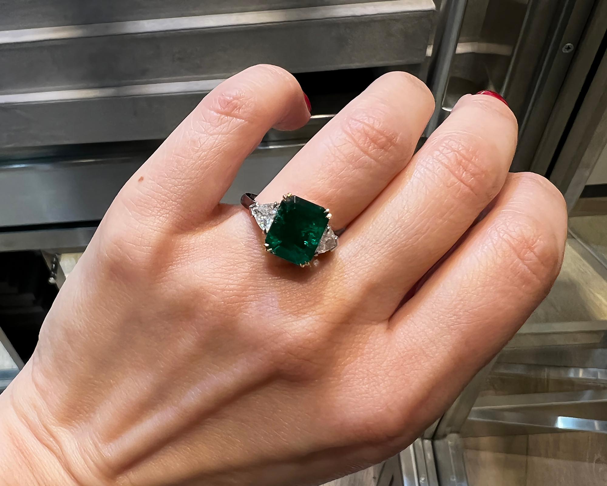 A cocktail ring featuring a 4.09 carat step-cut green emerald of Colombian origin. It's accompanied by the report from GRS stating that the emerald is Colombian Muzo green with minor clarity enhancement. 
2 triangular diamonds on both sides of the