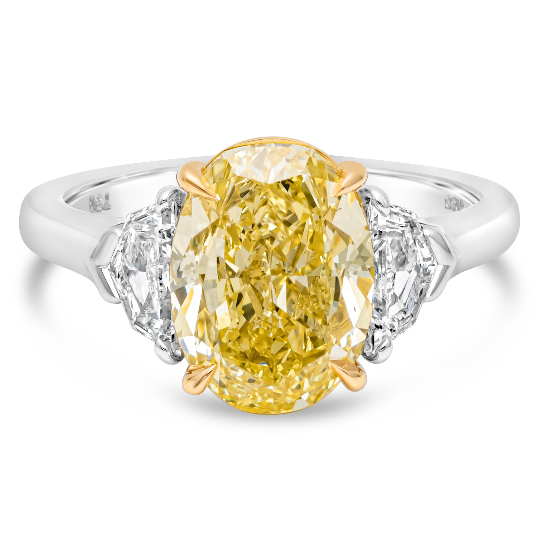 This wonderful and classy three stone engagement ring showcasing a GIA certified 4.12 carats oval cut color-rich fancy intense yellow diamond in the center, set in a four prong basket setting. Flanked by diamonds on each side weighing 0.60 carat