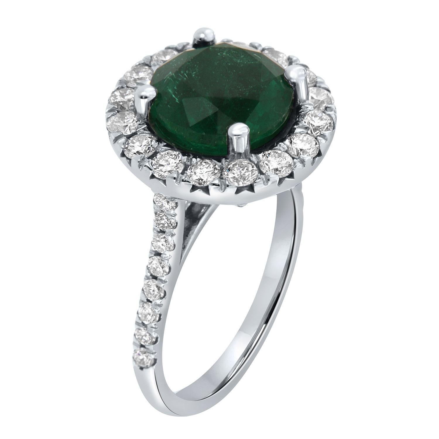 This 14k white gold ring features a RARE  4.14 Carat Round cut Natural Green emerald from Zambia. It is encircled by a halo of brilliant round diamonds on a 2.00 mm wide band. The diamonds are Micro-Prong set on 50% of the band.  The diamond's