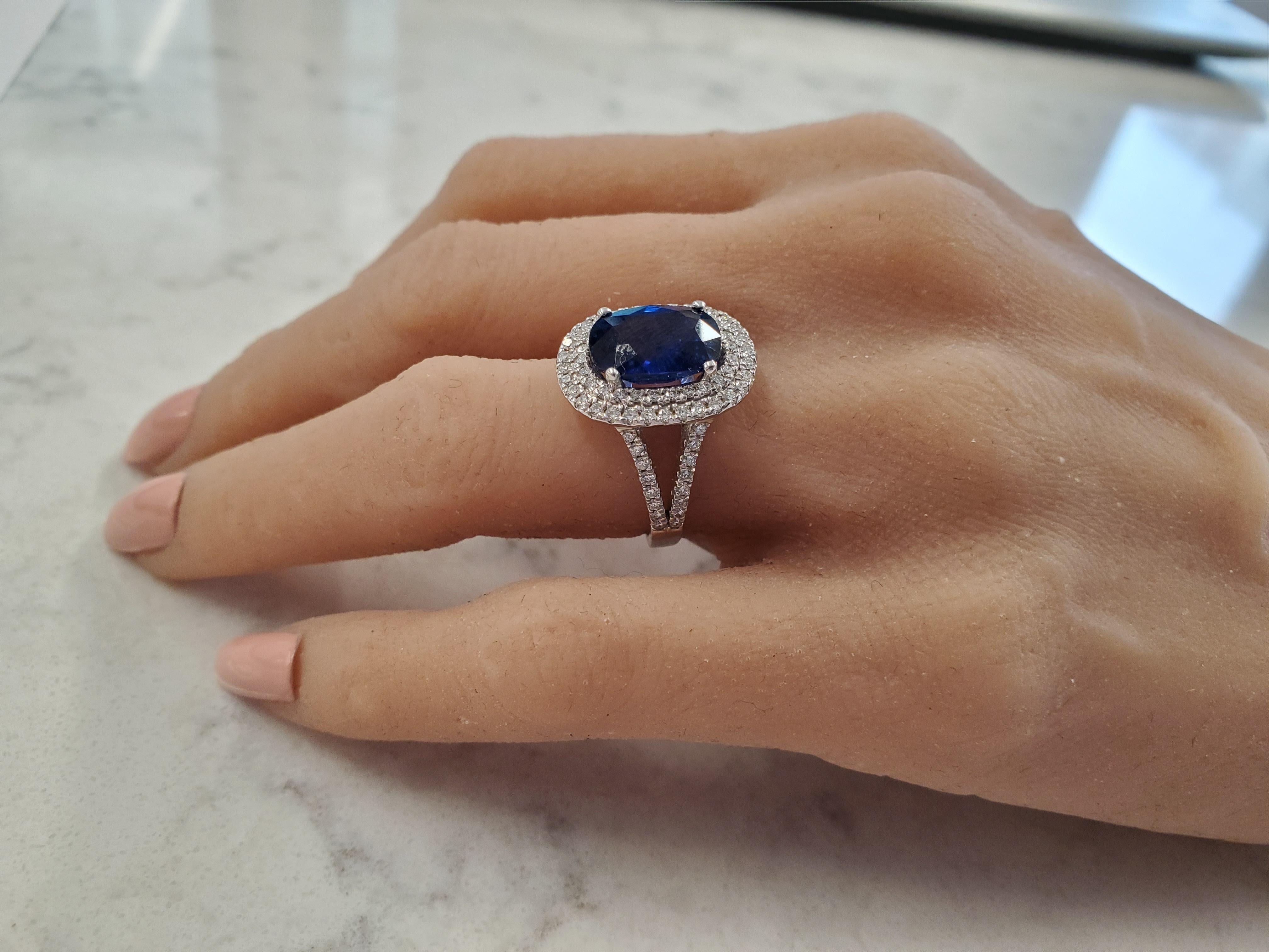 This opulent halo ring features a 4.49 carat cushion cut prong set blue sapphire that measures 11.62x8.27mm. The gem source is Sri Lanka; its color is royal blue, with excellent transparency and luster. This sapphire is surrounded by a double-decker