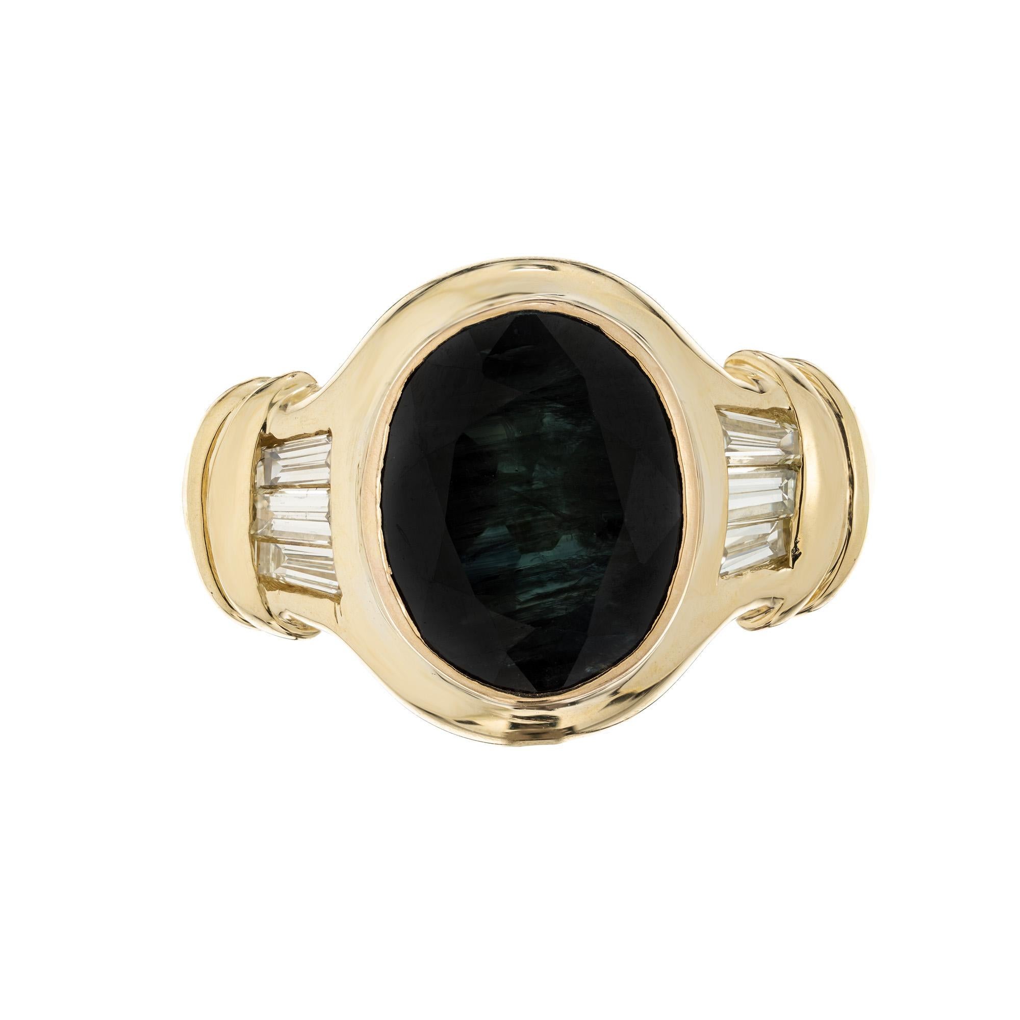1960's mid-century Greenish blue sapphire engagement ring. The center piece of this ring is a 4.53 oval bezel set greenish blue sapphire. Mounted int a 18k yellow gold setting and accented by 3 tapered baguettes on each side. The GIA has certified