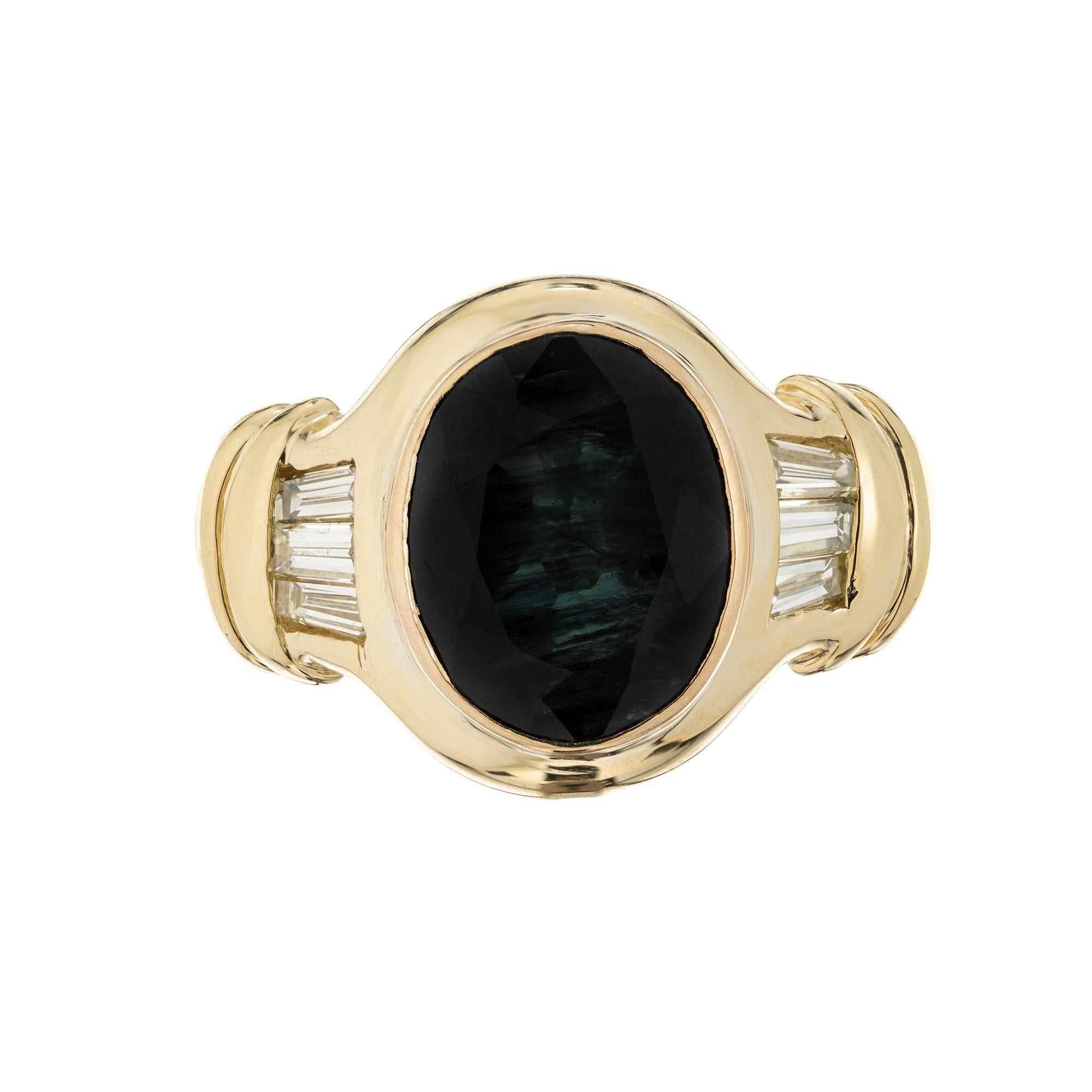 1960's mid-century Greenish blue sapphire engagement ring. The center piece of this ring is a 4.53 oval bezel set greenish blue sapphire. Mounted int a 18k yellow gold setting and accented by 3 tapered baguettes on each side. The GIA has certified
