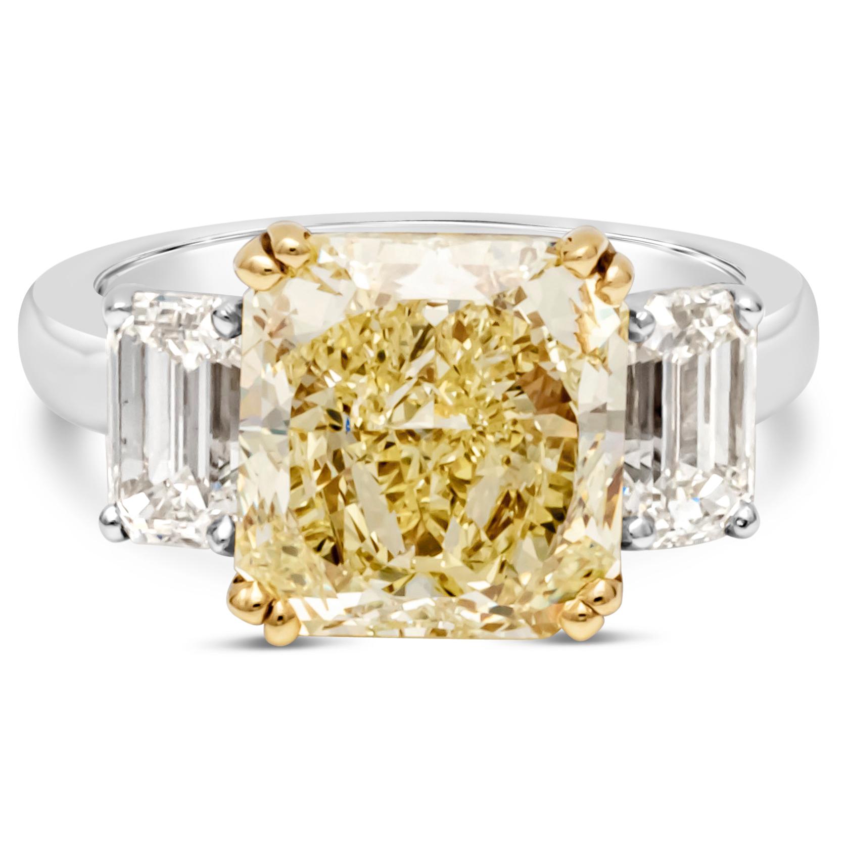 A color-rich three-stone engagement ring, showcasing a 4.68 carats radiant cut yellow diamond certified by GIA as Fancy Intense Yellow color and VS2 clarity, set in a timeless eight prong basket made of 18K yellow gold. Flanking the center diamond