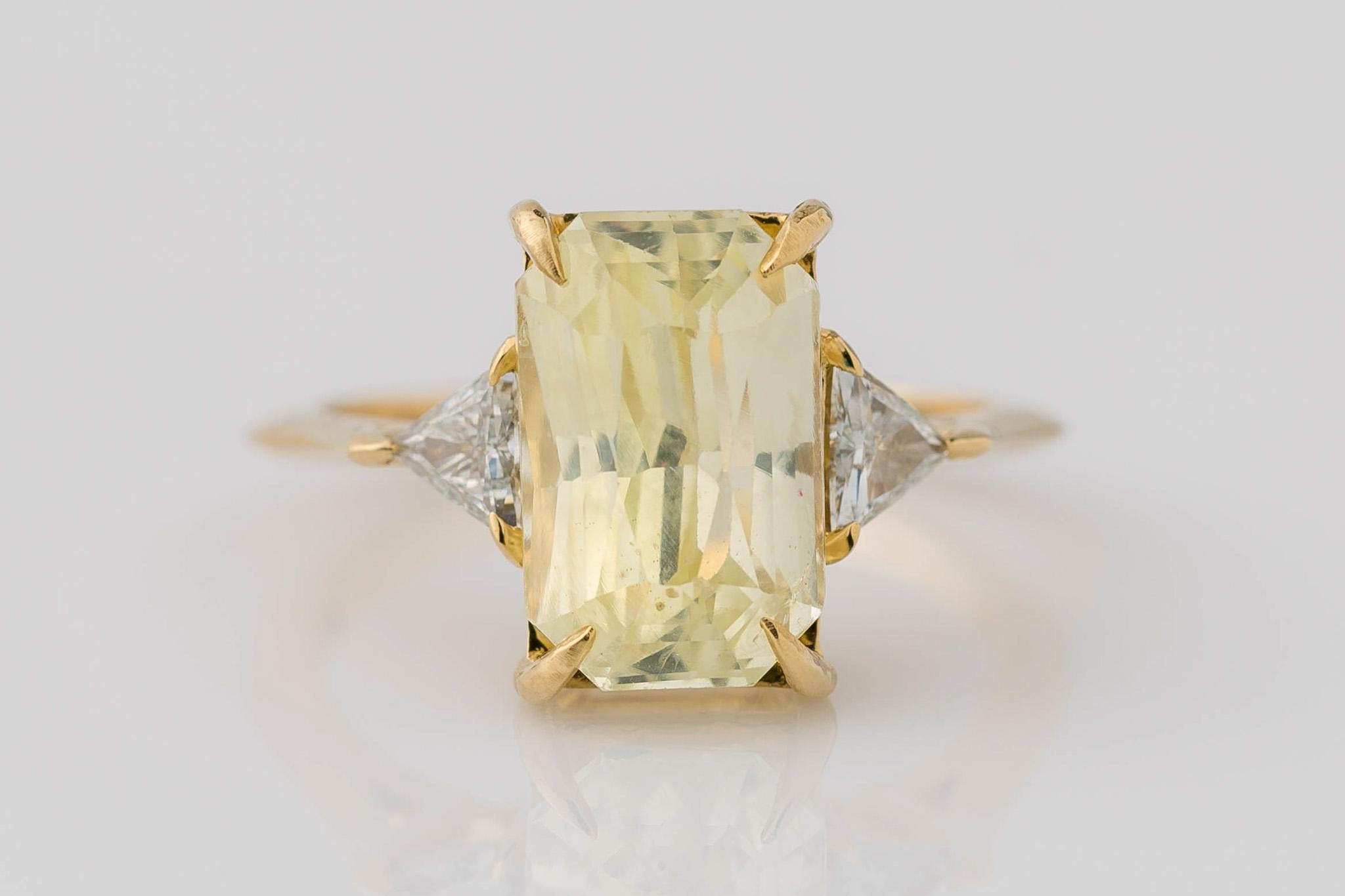 Experience unparalleled elegance with our 18K yellow gold 3-stone radiant cut yellow sapphire diamond ring. The centerpiece, a completely natural and rare unheated sapphire weighing 4.73 carats, features a captivating light-yellow hue and measures