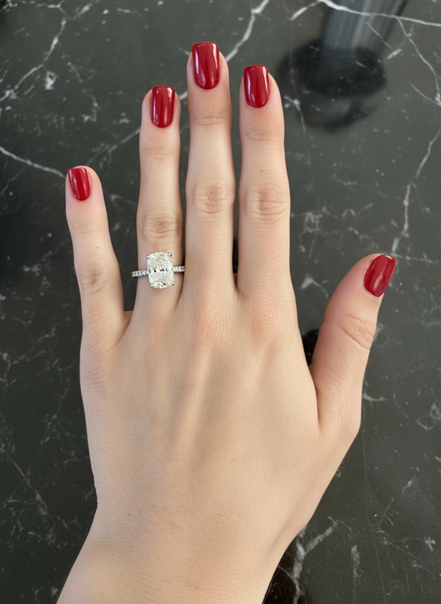 Este magnífico anillo gira en torno a un diamante de talla brillante modificado en cojín, certificado por el GIA, de 5 quilates, graduado en color D y claridad VS2, una rara combinación que garantiza tanto una blancura excepcional como un brillo