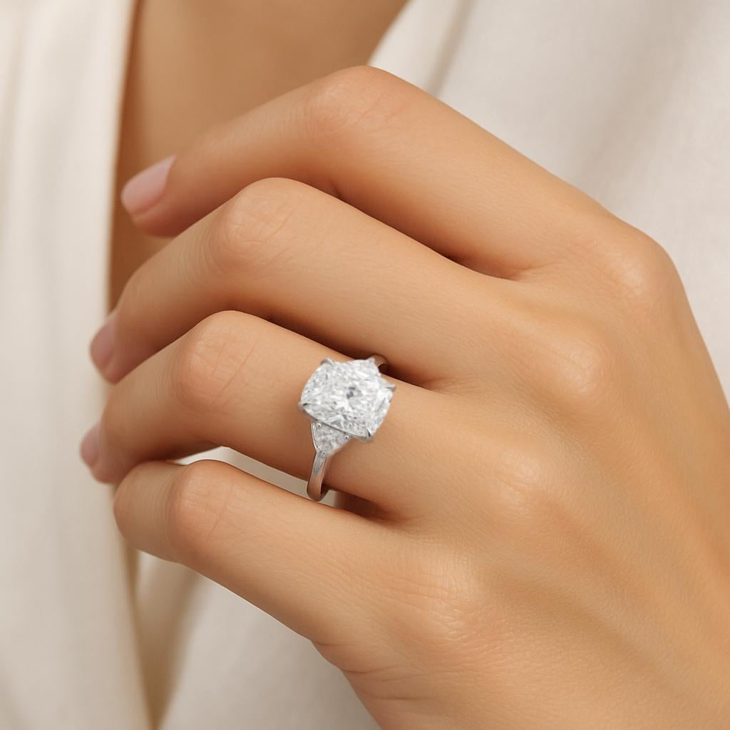 This graceful engagement ring showcases a GIA certified 5.01 carat cushion cut diamond set in platinum, offering a timeless blend of softness and brilliance. 

The central stone presents a bright F color grade, delivering near colorless beauty with