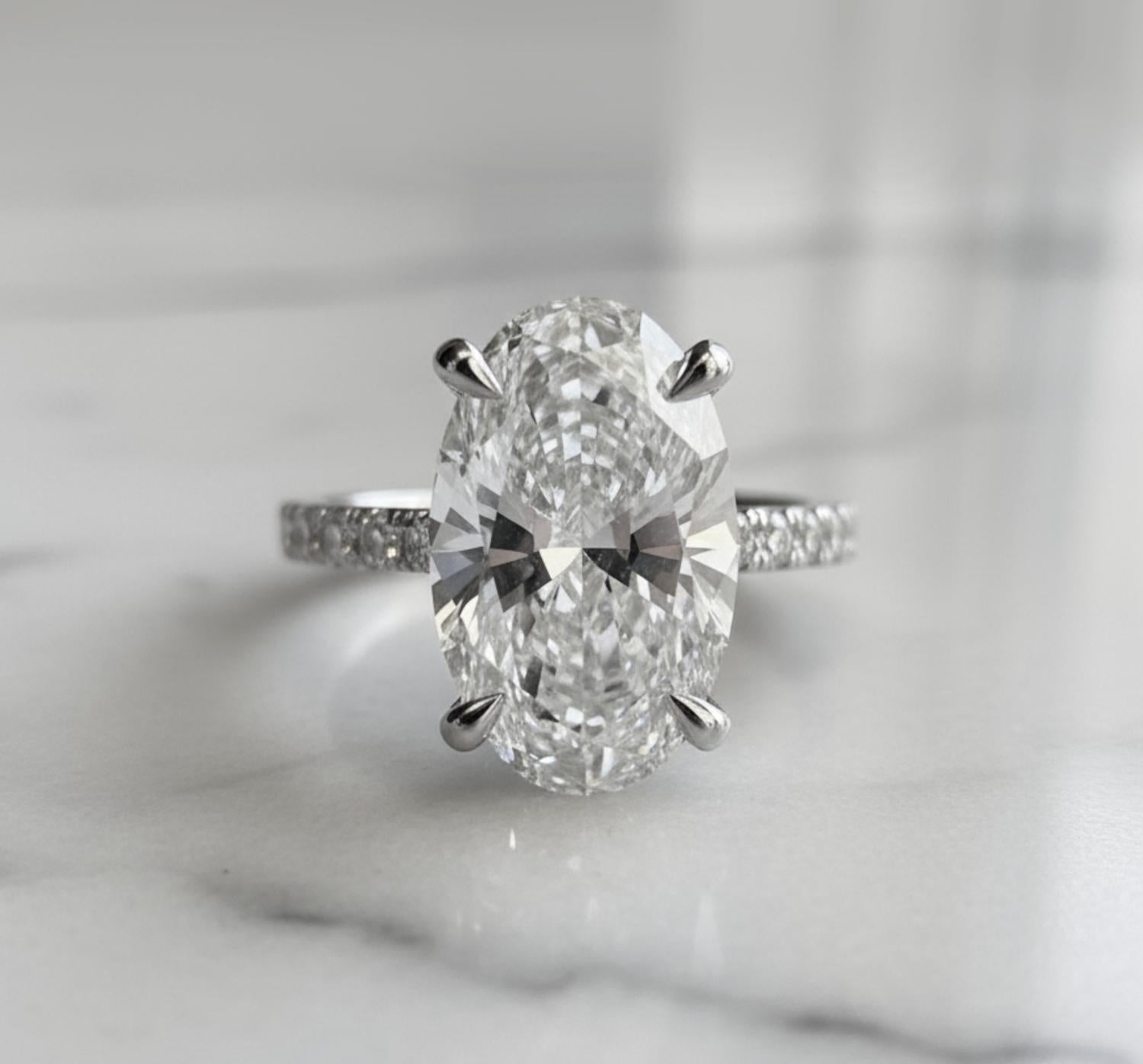 Une bague de fiançailles extraordinaire mettant en valeur un superbe diamant ovale de 5 carats certifié par le GIA, de couleur E et de pureté VS1. Ce diamant exceptionnel affiche une brillance et une symétrie remarquables, offrant une forme allongée