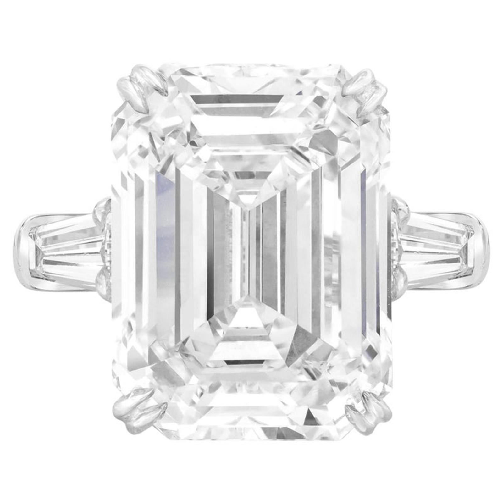 This extraordinary engagement ring showcases a breathtaking 5.01 carat emerald-cut diamond, GIA certified for its remarkable quality. The elegant step-cut facets of the center stone create a mesmerizing hall-of-mirrors effect, emphasizing clarity