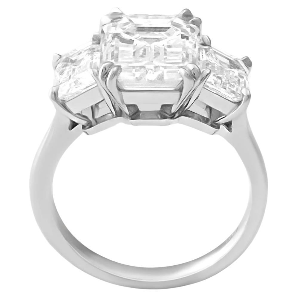 This GIA certified three stone ring features a captivating 5 Carat Emerald Cut diamond as its centerpiece, flanked by two smaller emerald-cut diamonds, all set in 18k white gold. 

The central diamond has a stunning F color grade, offering