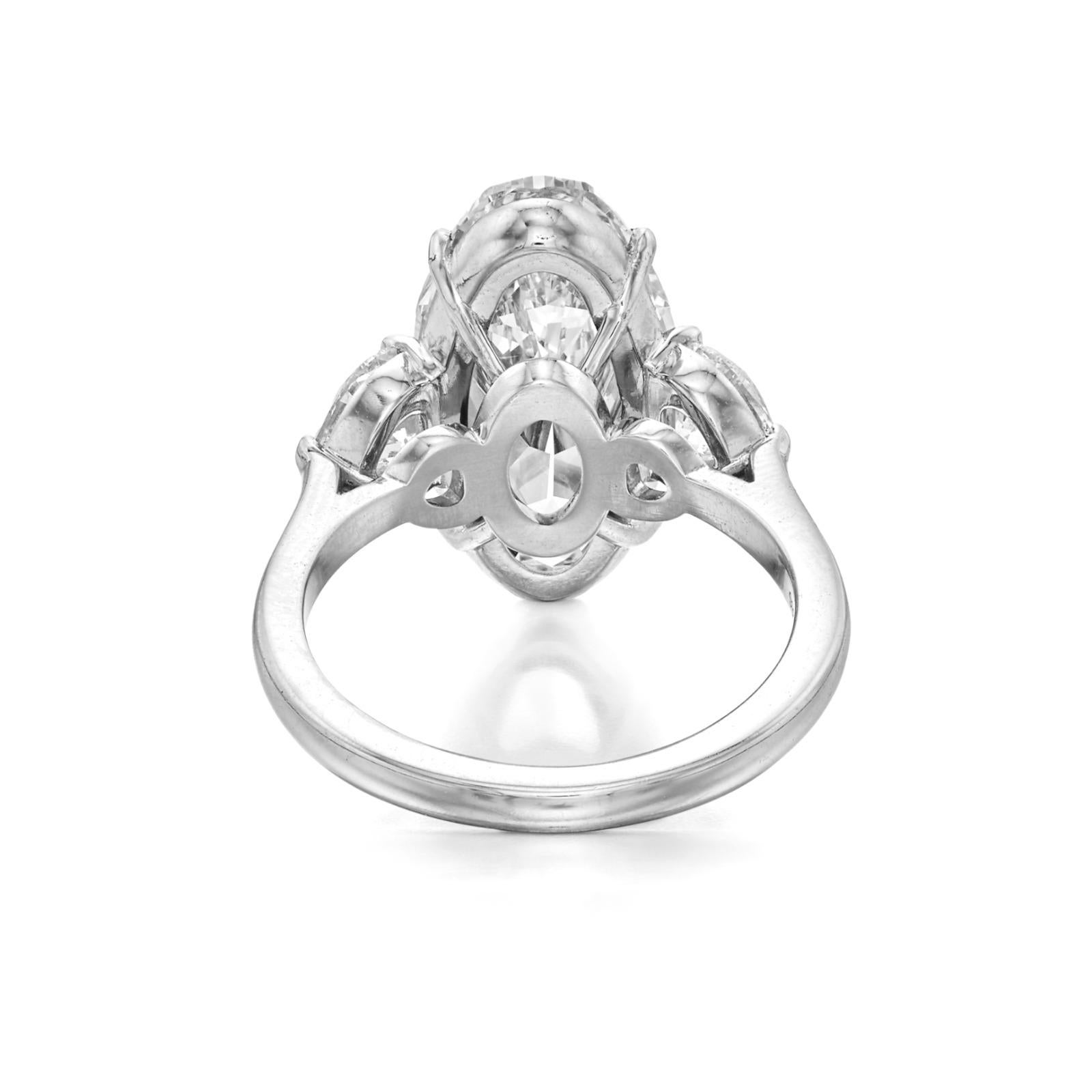 Cette bague de fiançailles magnifiquement travaillée présente un diamant de taille ovale de 5,10 carats en guise de pièce maîtresse, accentué par deux pierres latérales en forme de poire qui créent une silhouette gracieuse et effilée. Serti dans du