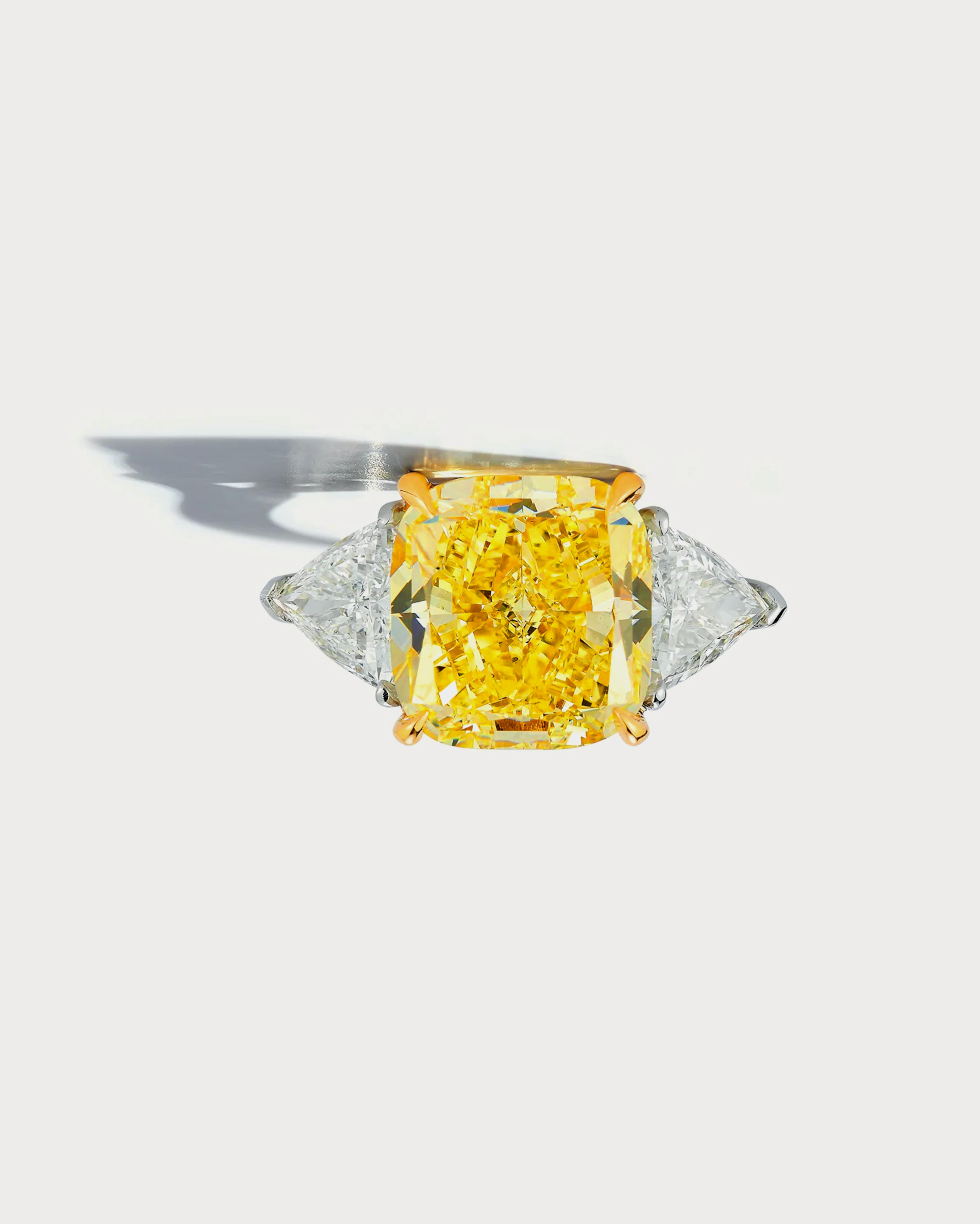 Cette élégante bague est ornée d'une superbe pierre centrale de 5 carats de couleur jaune fantaisie, taillée en coussin, complétée par deux autres pierres en diamant. Fabriquée par des experts, cette bague présente un design exquis et un poids en