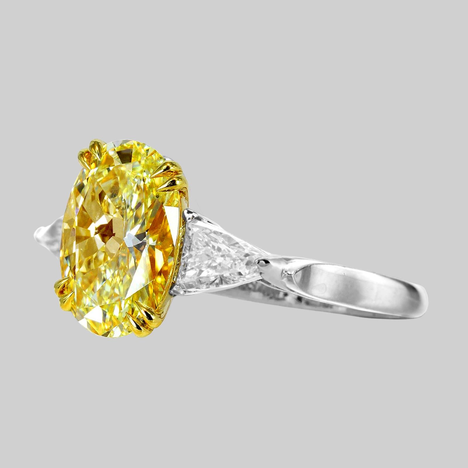 Questo affascinante anello mette in mostra uno splendido diamante giallo fantasia di 5 carati con taglio ovale come centro, affiancato da due eleganti diamanti con taglio trilione. 

Il diamante centrale, con la sua vibrante tonalità gialla, emana