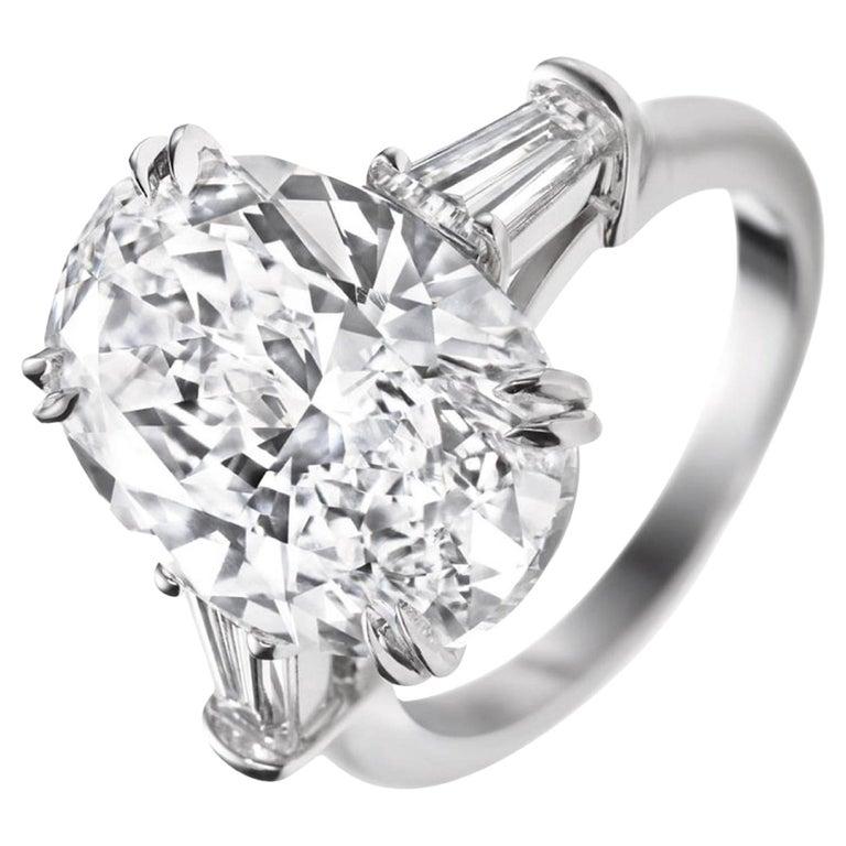 Questo splendido anello di fidanzamento a tre pietre presenta un notevole diamante ovale da 5.01 carati come centro, affiancato da due eleganti diamanti baguette affusolati. 

Il diamante centrale ha un grado di colore H, con una luce morbida e