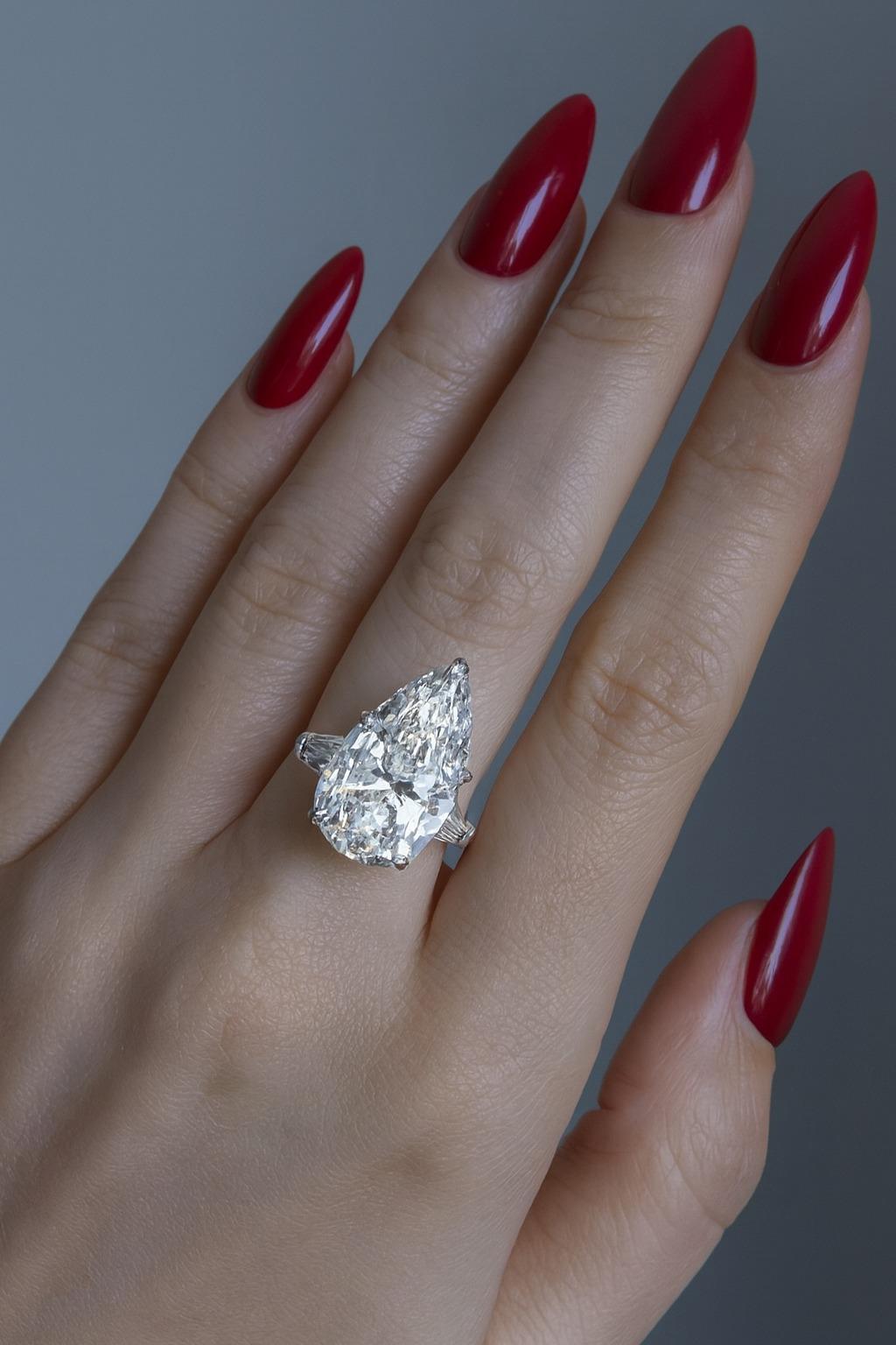 Un capolavoro di raffinatezza e maestria, questo anello di fidanzamento in platino con tre pietre è una testimonianza di perfezione. Al centro brilla uno straordinario diamante naturale a forma di pera con taglio brillante da 5 carati. Classificato