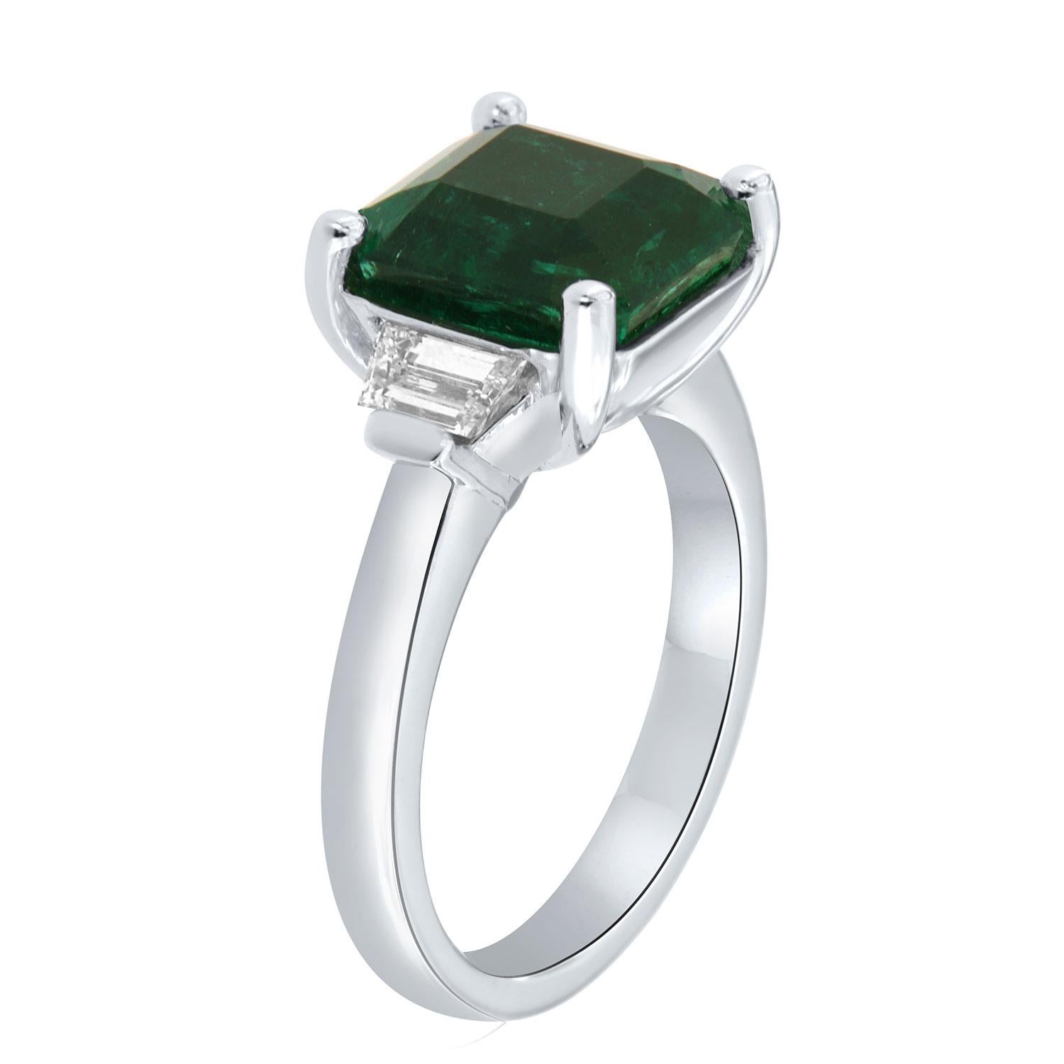 This classic Three-Stone Platinum ring features a 5.00 Carat Asscher cut Vibrant green Natural Emerald flanked by two(2) Trapeze shaped diamonds in a total weight of 0.55 Carat on a 2.8 mm wide band.
This Zambian Emerald exhibits a vibrant green