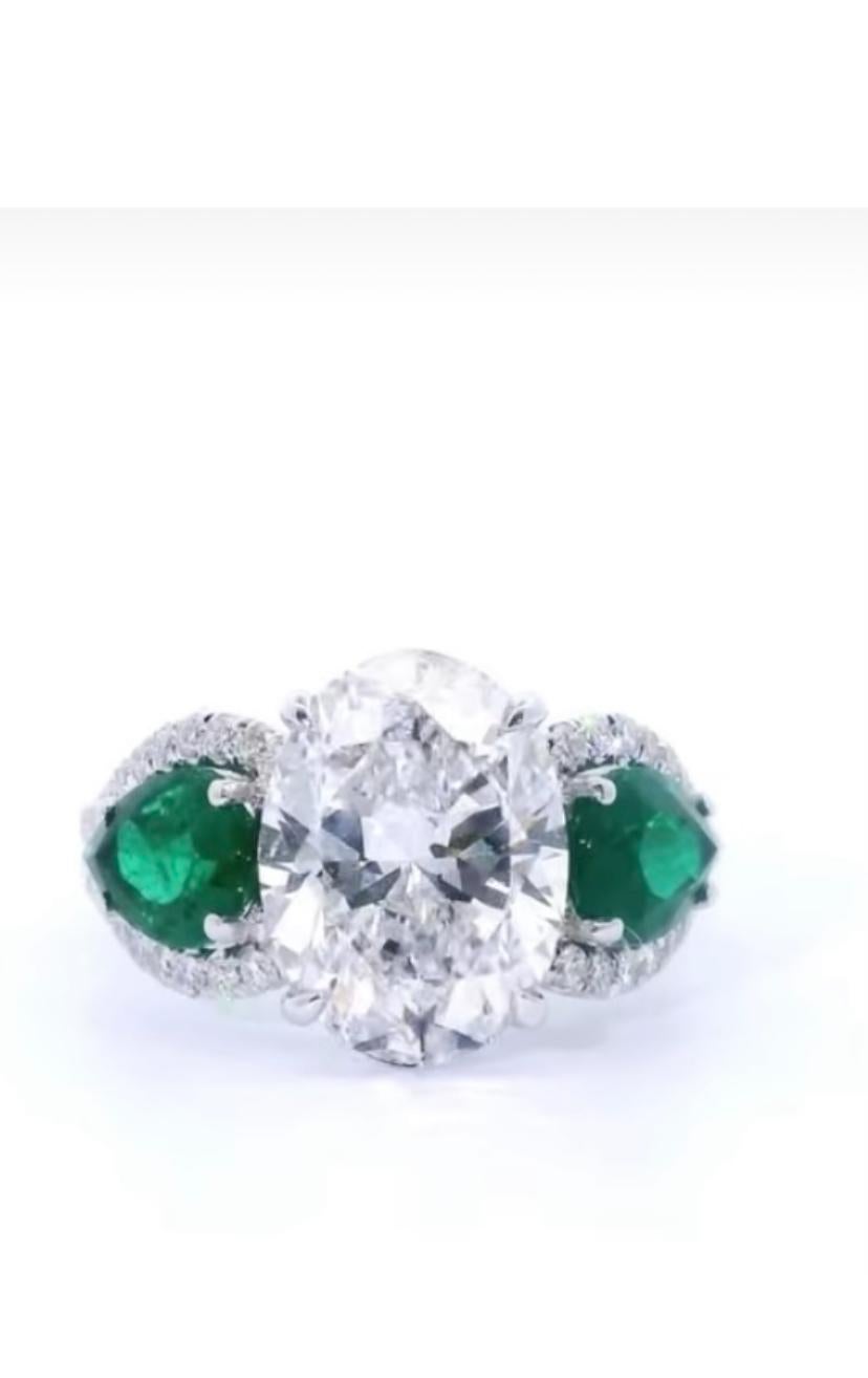 Ein exquisites Gleichgewicht von Eleganz und kräftiger Farbe.
Dieses individuelle Design zeichnet sich durch einen atemberaubenden ovalen Diamanten in der Mitte aus, der von zwei lebhaften Smaragden an den Seiten flankiert wird. Ein zeitloses Stück