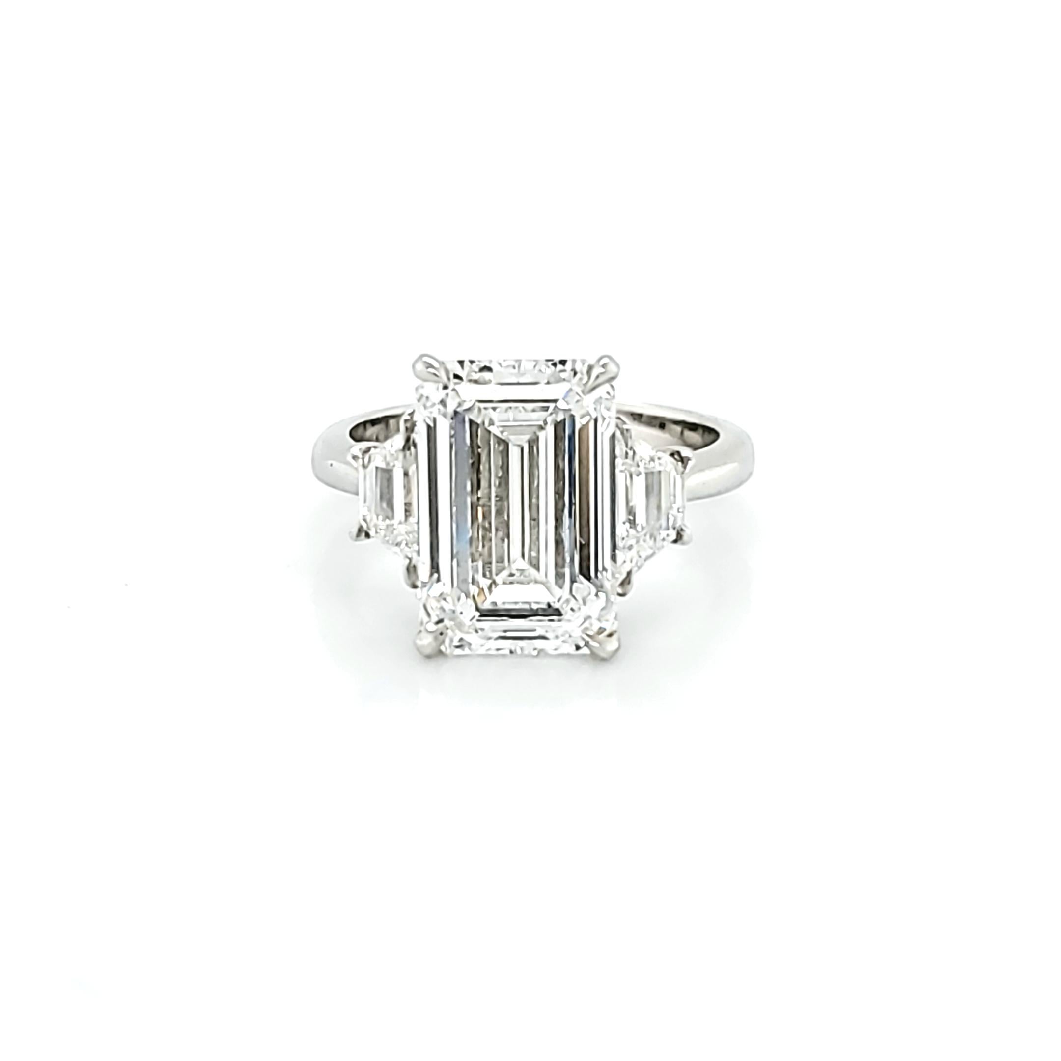Center stone is a 5.01 carat E color internally Flawless Clarity. Set in a handmade platinum setting with 2 trapezoid shaped diamonds weighing 0.73 carats total and are of similar color/clarity to the Emerald Cut. 1.50 ratio makes this emerald cut a