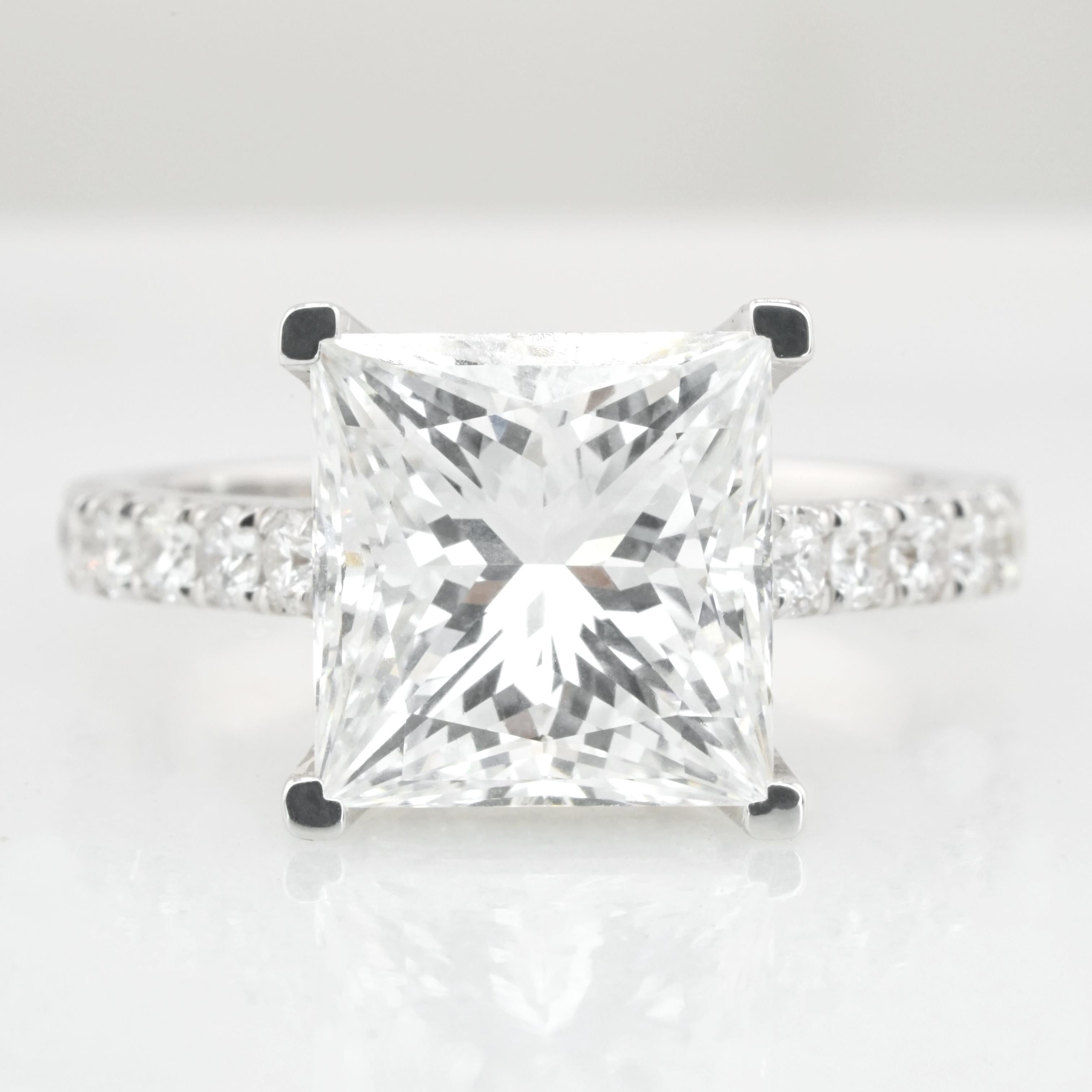This stunning ring features a GIA certified 5.01 carat princess cut diamond, set in an 18K white gold band adorned with pavé diamonds. 
The center diamond has a color grade of H and a clarity grade of VVS1, ensuring impressive quality and