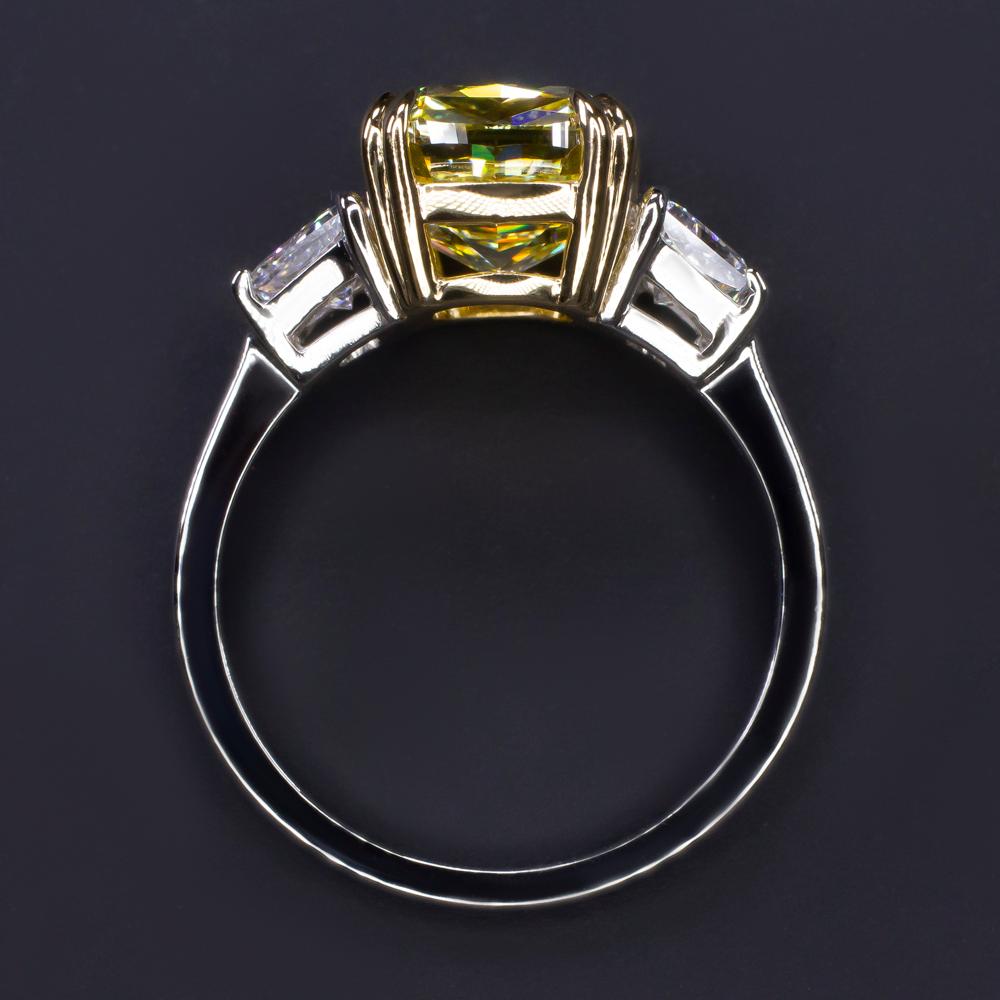 This exquisite engagement ring showcases a 5.02 carat fancy yellow diamond, set in a striking blend of 18K white gold and 18K yellow gold. 

The central diamond’s delicate and luminous hue exudes elegance and sophistication. With a clarity grade of