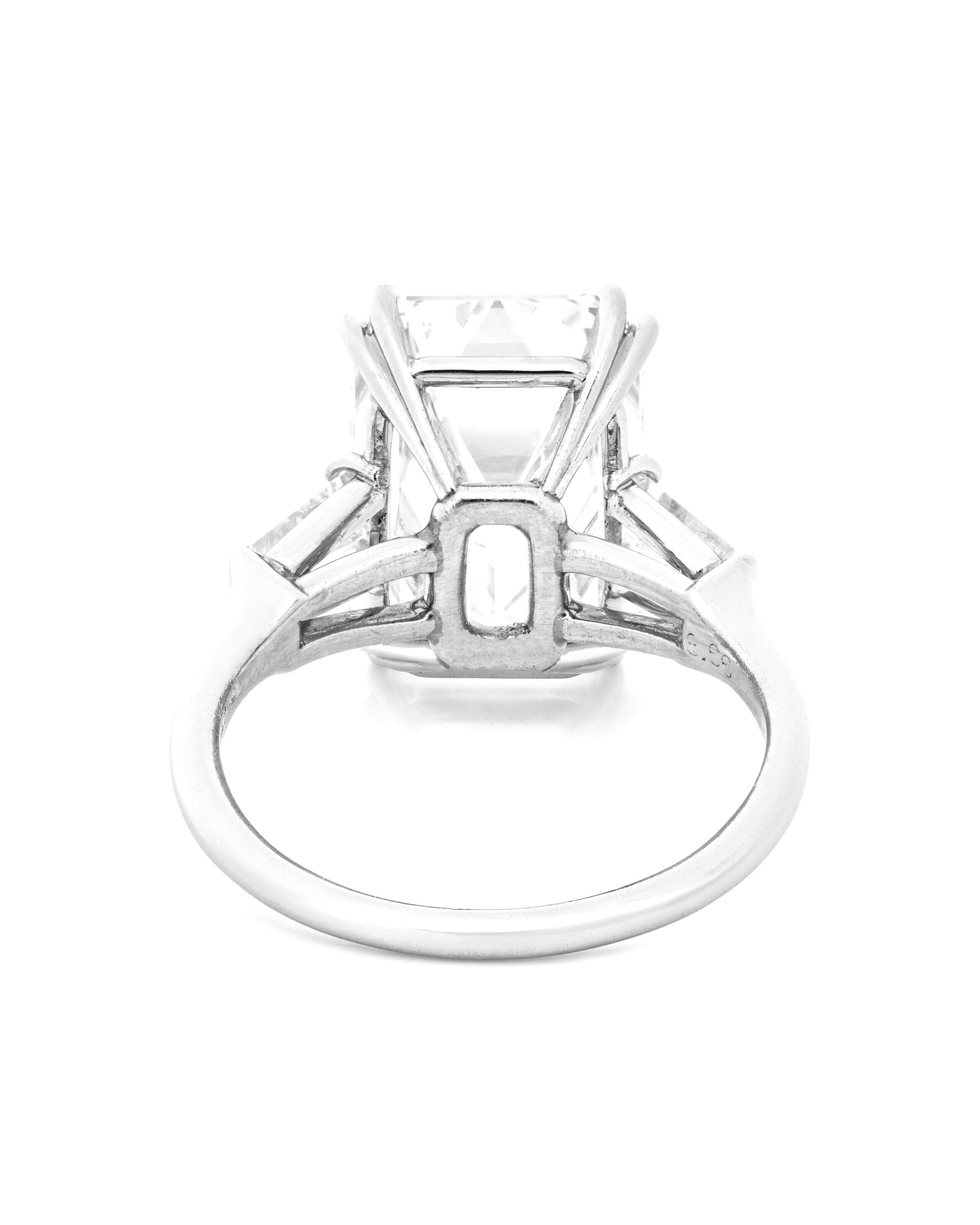 classic engagement ring features a substantial 5.01 carat emerald cut diamond, elegantly flanked by a pair of trapezoid diamonds, all set in a sleek platinum band. The center diamond has GIA certification and is graded with a nice white G color,