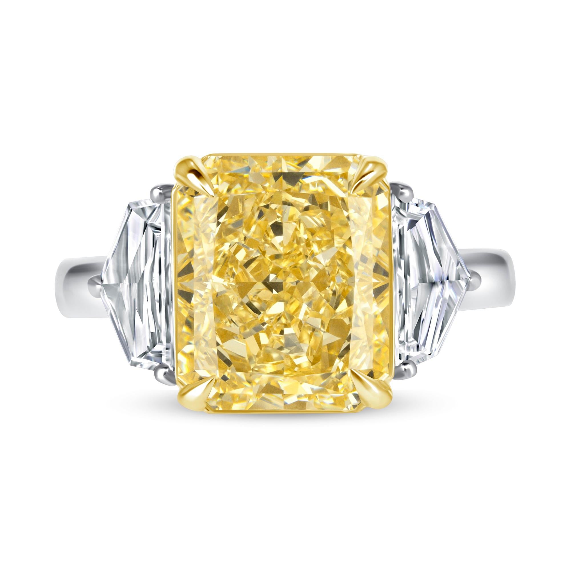 Este anillo de tres piedras tiene un diamante talla Radiante Amarillo Fancy de 5,24 quilates con certificado GIA de claridad VVS2 y dos diamantes talla Cadillac, de color E-F y claridad VS1 engastados en Oro Amarillo de 18 quilates y Platino.  Tiene