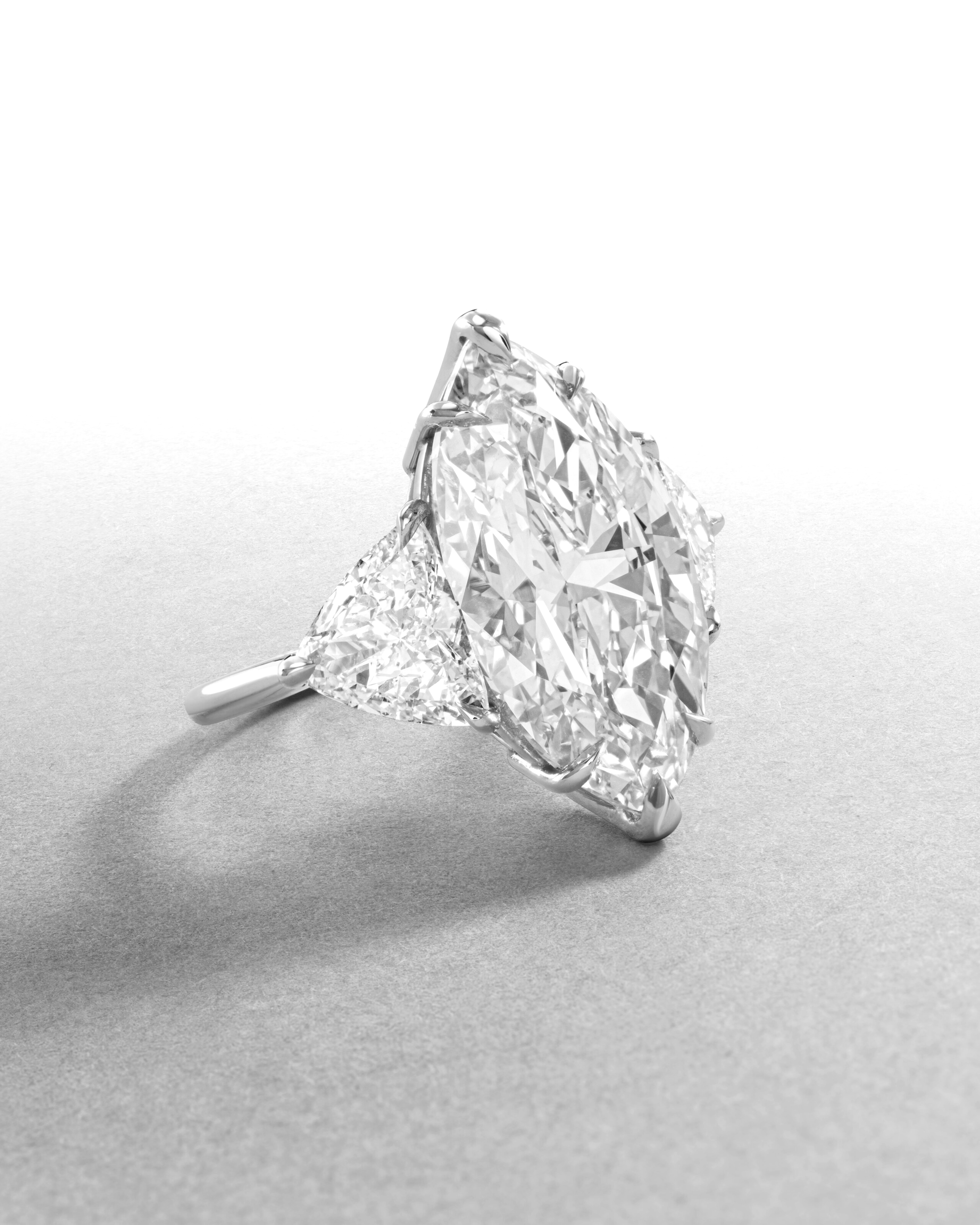Cette bague en platine à trois pierres, à la fois audacieuse et gracieuse, met en valeur un spectaculaire diamant Marquise Brilliante de 5,31 carats certifié par la GIA, flanqué de deux diamants latéraux de taille trillion parfaitement assortis,