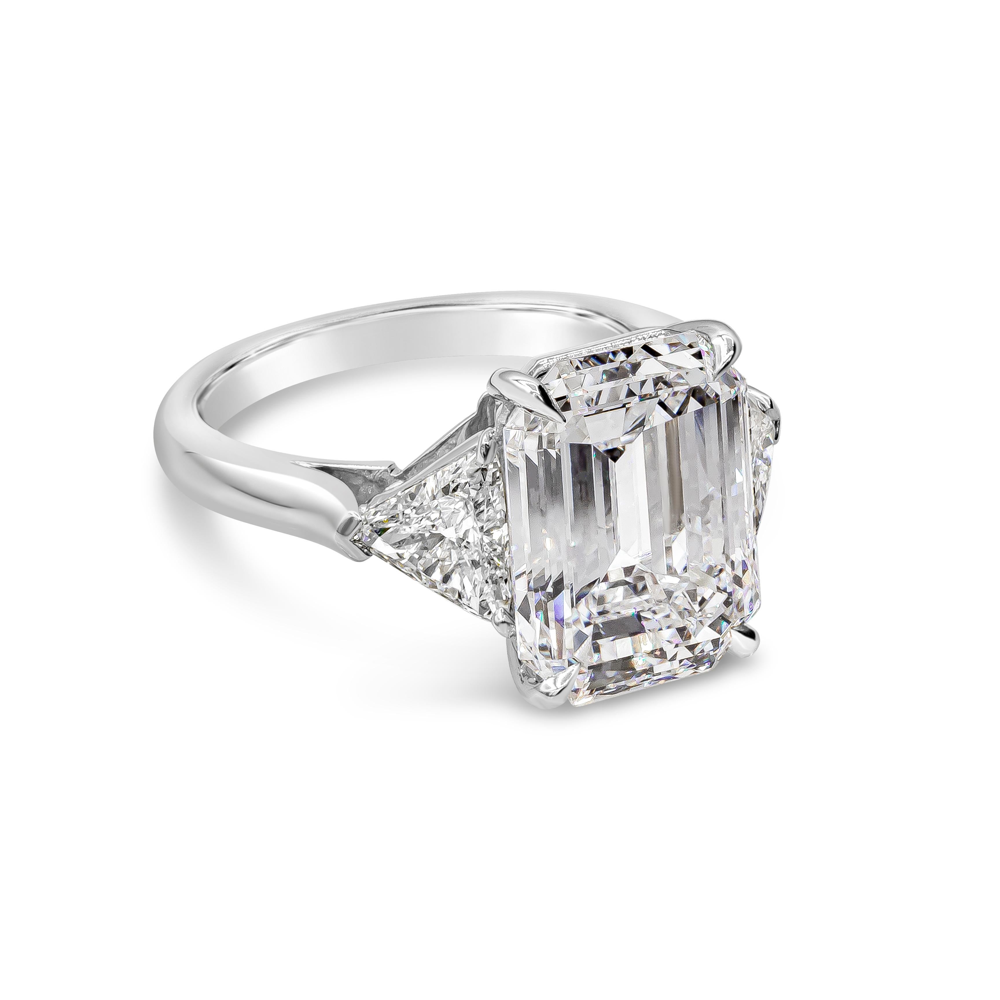 A beautiful three-stone engagement ring, showcasing a 5.46 carats emerald cut diamond certified by GIA as F color and VS2 clarity, set on a four prong setting. Flanked by two trillion brilliant cut diamonds weighing 1.01 carats total. Finely made