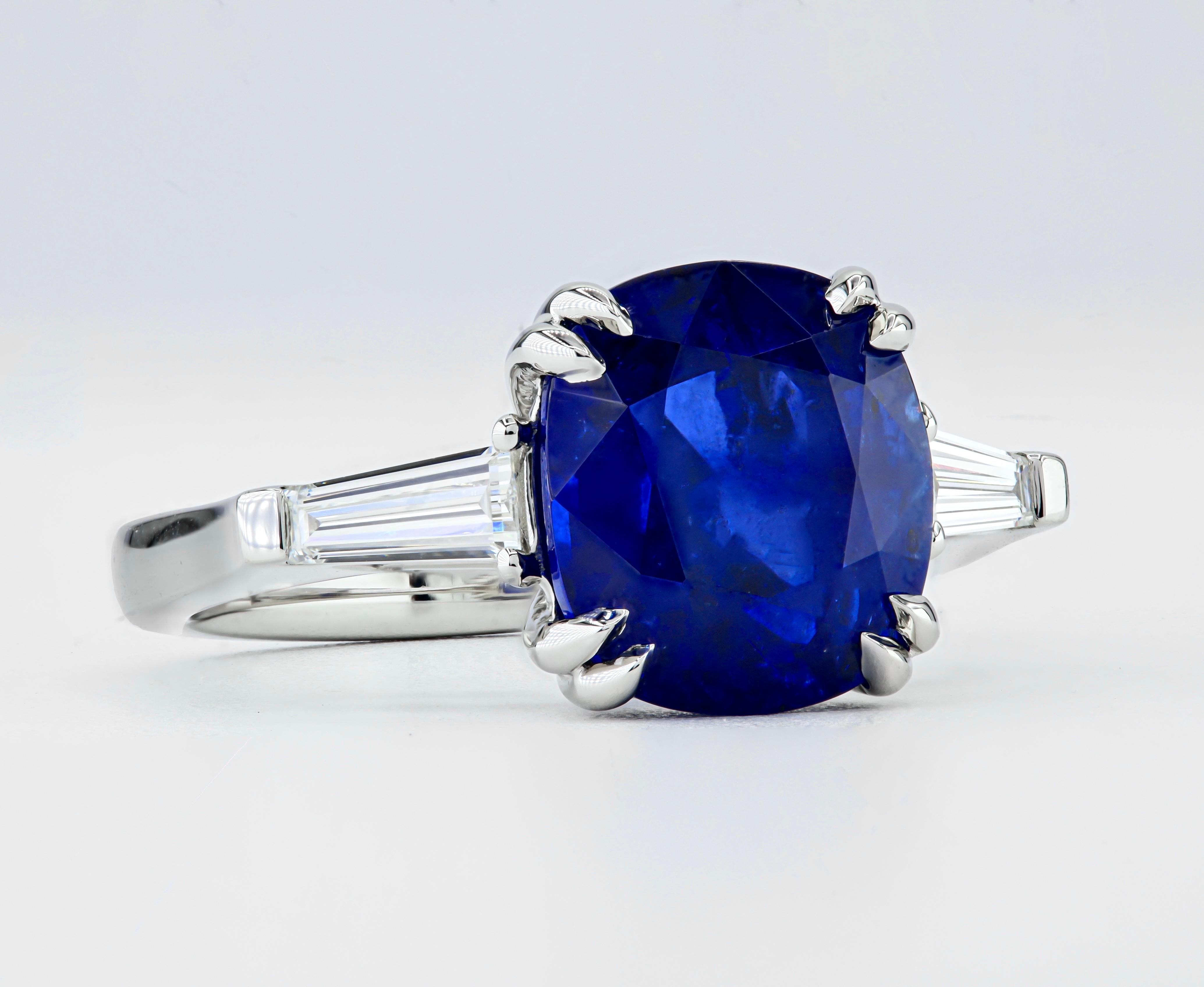 This expertly crafted ring features a GIA Certified 5.54ct Luscious/Vibrant Blue Sri Lankan Sapphire, securely nestled in a comfortable fit Platinum three-stone setting. It is elegantly complemented by a pair of exquisite E/F VS+ Tapered Baguette