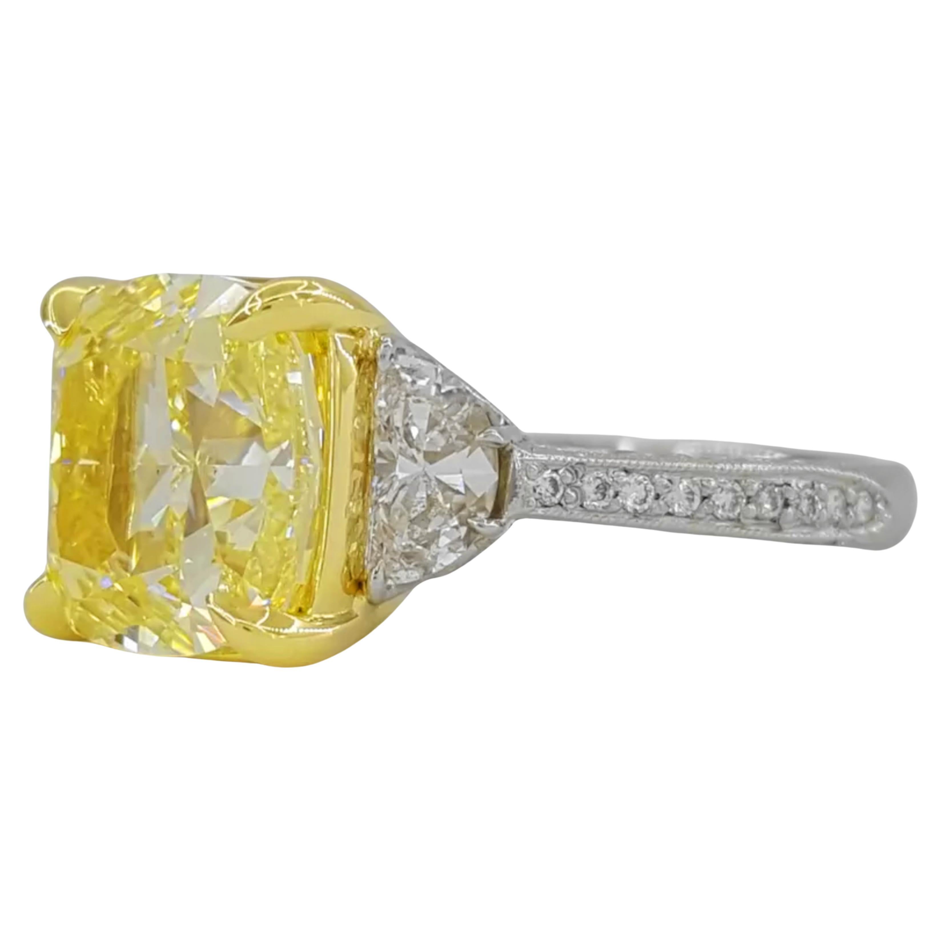 5.67 ct total weight cushion brilliant cut natural yellow diamond three-stone engagement ring is a stunning piece that combines platinum and 18K yellow gold. The centerpiece is a 5.01 ct natural cushion brilliant cut diamond, characterized by a Y to