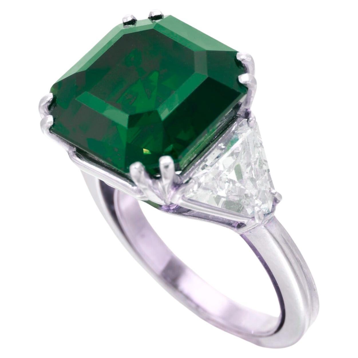a breathtaking masterpiece: a 5.70 carat natural emerald radiating with unparalleled beauty. This exquisite gemstone is elegantly set in a solid platinum ring, flanked by two stunning trillion-cut diamonds, each certified by GIA for their