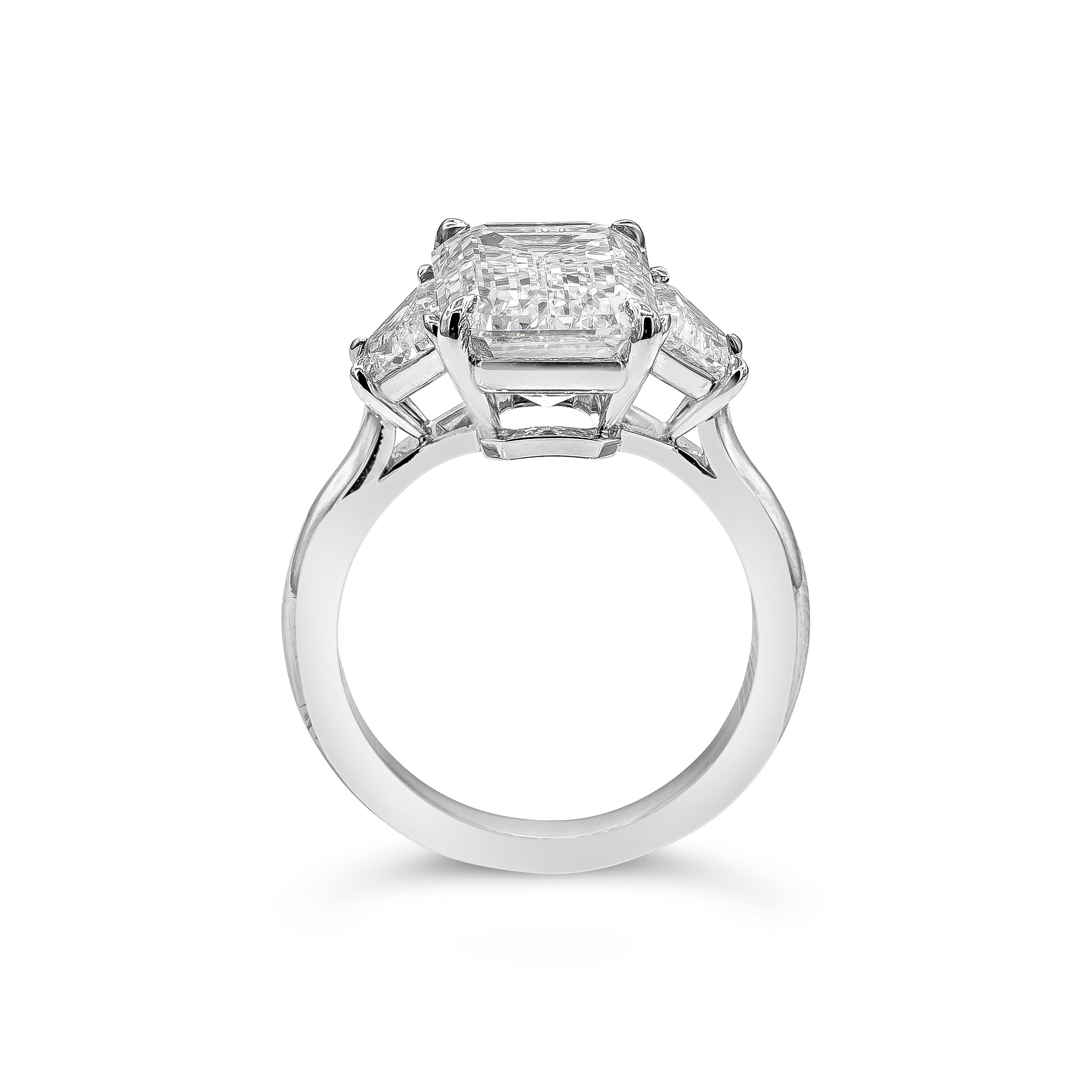 A classic and timeless engagement ring style showcasing a long emerald cut diamond weighing 5.80 carats and certified by GIA as I color, VVS1 clarity. Center diamond is flanked by two trapezoid diamonds weighing 0.88 carats total. Made in