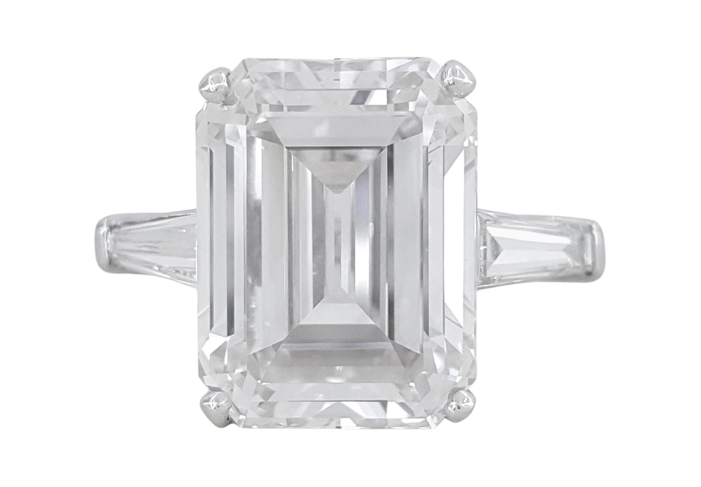 This remarkable engagement ring features a stunning 6 carat emerald-cut diamond, GIA certified for its exceptional quality. The elongated shape and step-cut facets of the center stone create a mesmerizing hall of mirrors effect, emphasizing depth