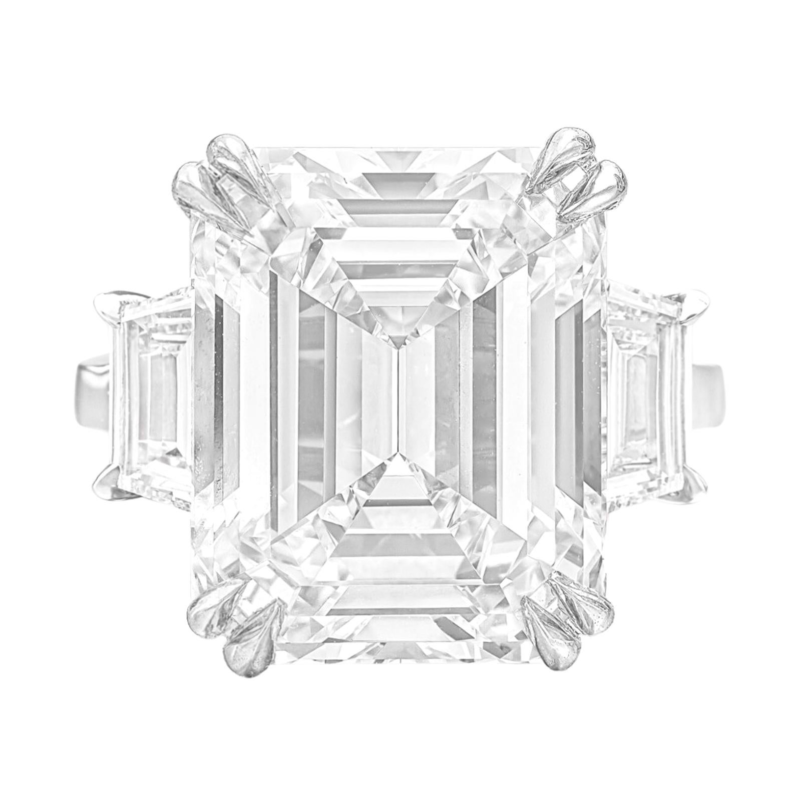 This remarkable ring showcases a breathtaking 6-carat emerald-cut diamond set gracefully in an exquisite 18-karat white gold band adorned with trapezoid-cut diamonds. The central diamond, an awe-inspiring 6-carat gem, boasts an exceptional G color