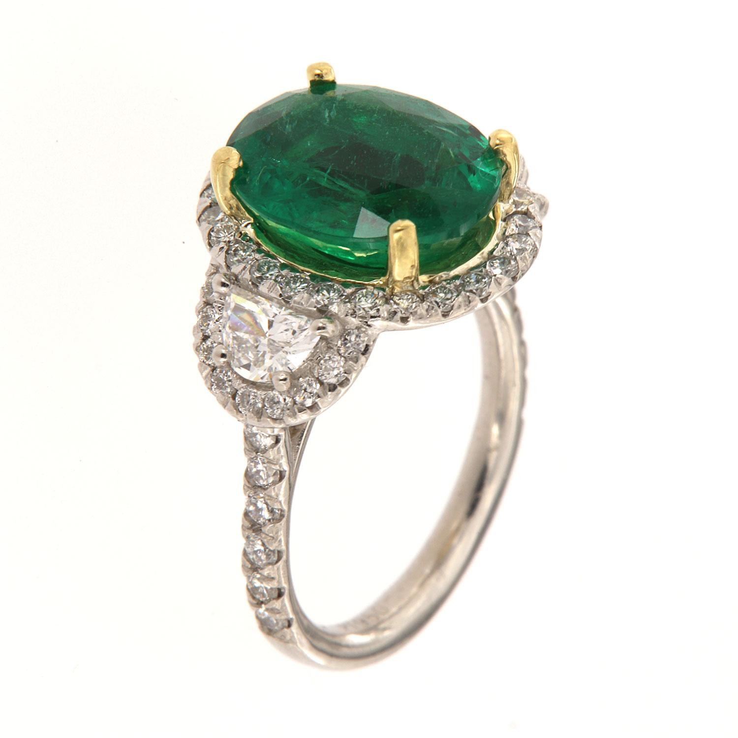 This Platinum and 18K Yellow Gold ring feature a 6.00 Carat Oval shaped Natural Emerald from Zambia in a vibrant green color encircled by a halo of brilliant round diamonds and flanked by two (2) Half-Moon shape diamonds wrapped with delicate
