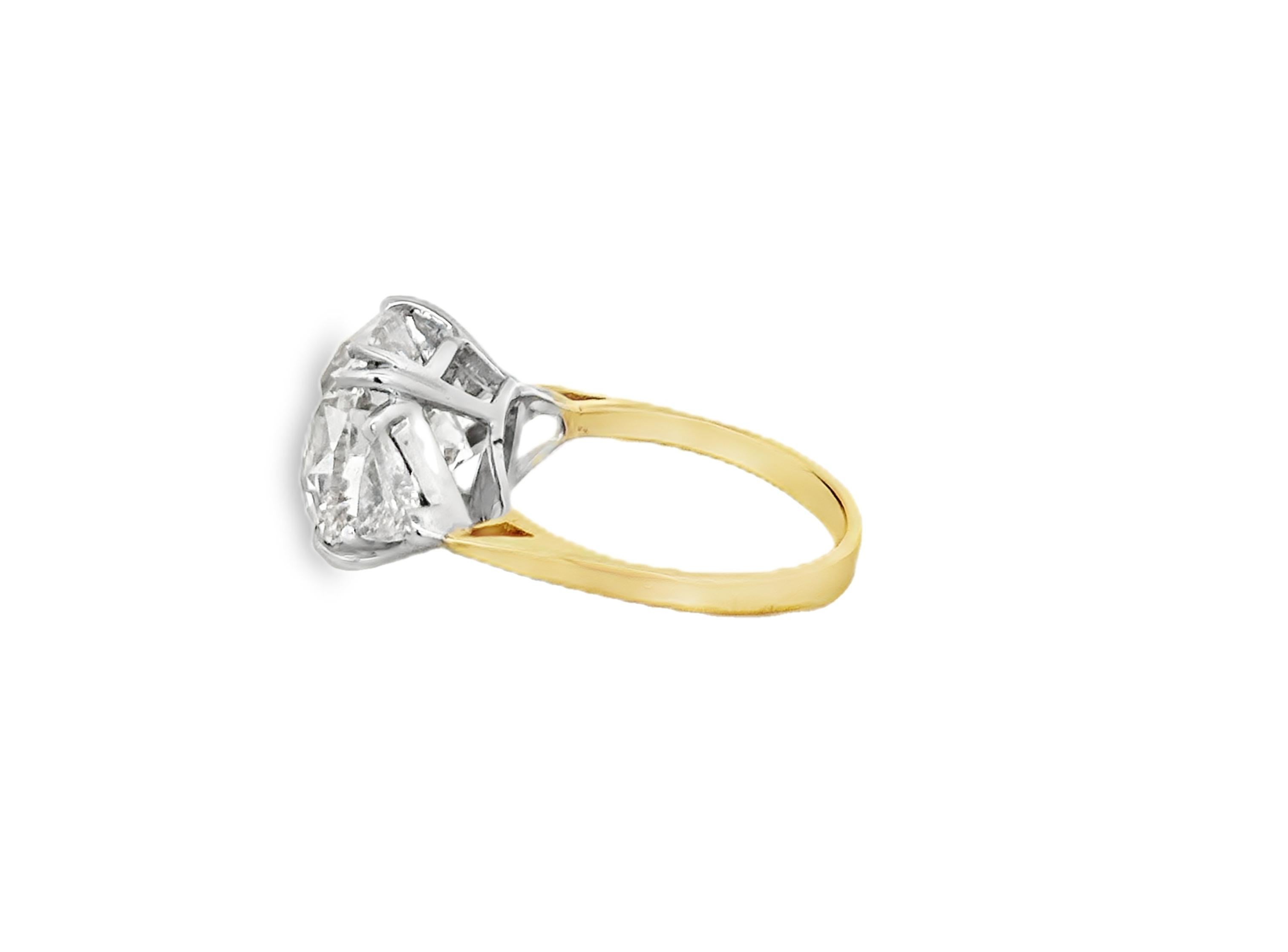 Questo squisito anello di fidanzamento presenta uno splendido diamante centrale da 6,11 carati con taglio a cuscino, certificato GIA, con grado di colore L e purezza SI2. Affiancato da eleganti pietre laterali a forma di triangolo, questo pezzo