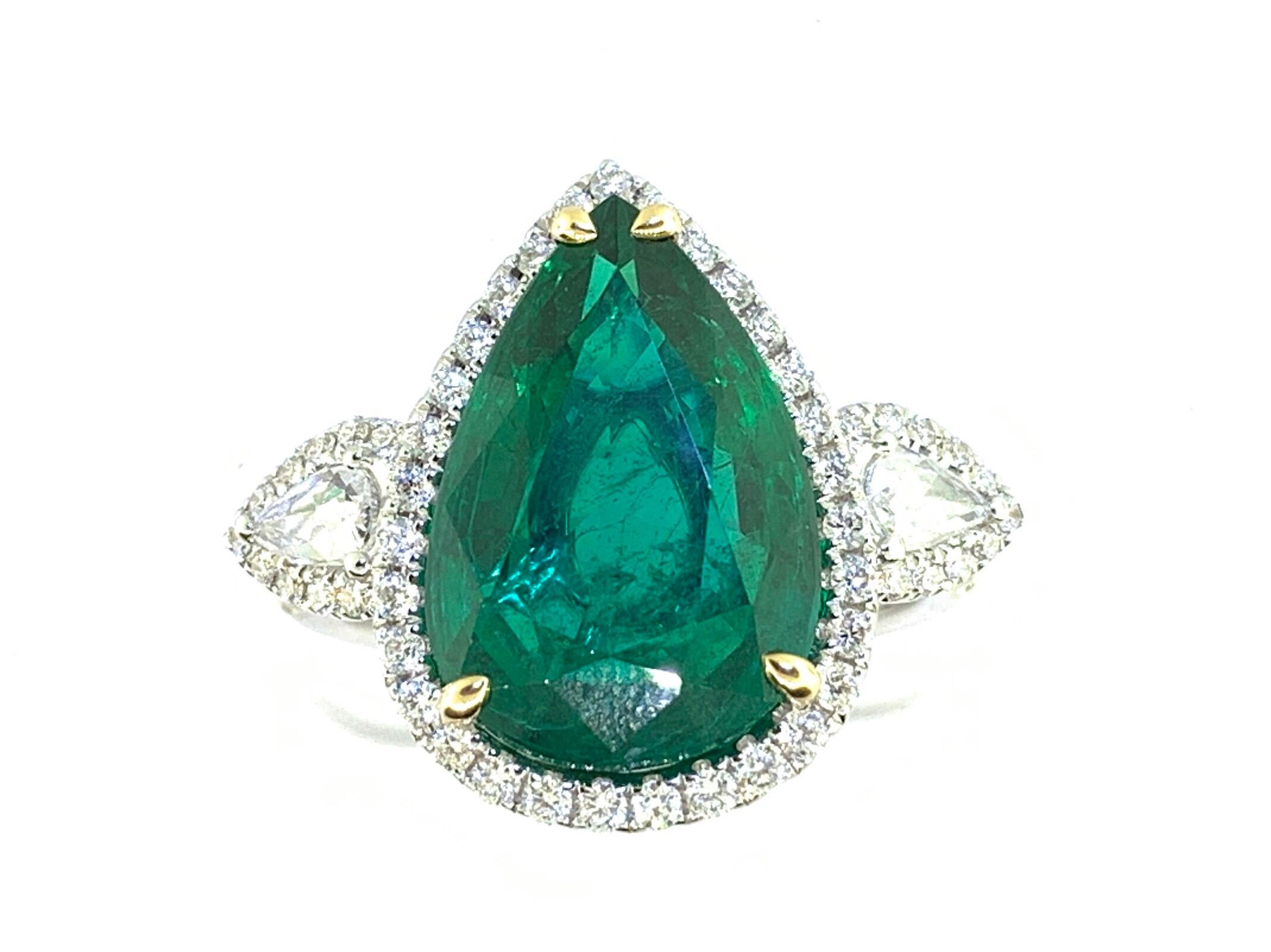 This stunning cocktail ring showcases a beautiful GIA Certified 6.21 Pear Shape Emerald with a Diamond Halo. The Emerald is flanked by two Rose Cut Diamonds, and is set in 18k white gold, with 18k yellow gold prongs on the Emerald. Total diamond