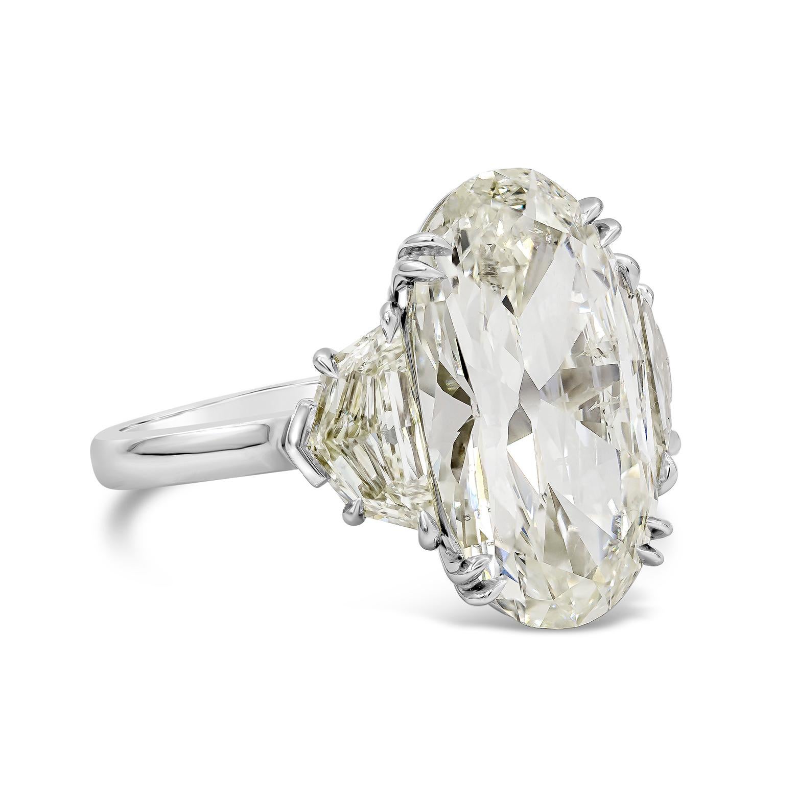 Features an elongated oval cut diamond weighing 6.45 carats, accented by epaulet diamond on each side. Accent diamonds weigh 1.55 carats total. GIA certified the center diamond as L color, SI2 clarity. Set in a Polished Platinum mounting. Size 6.25