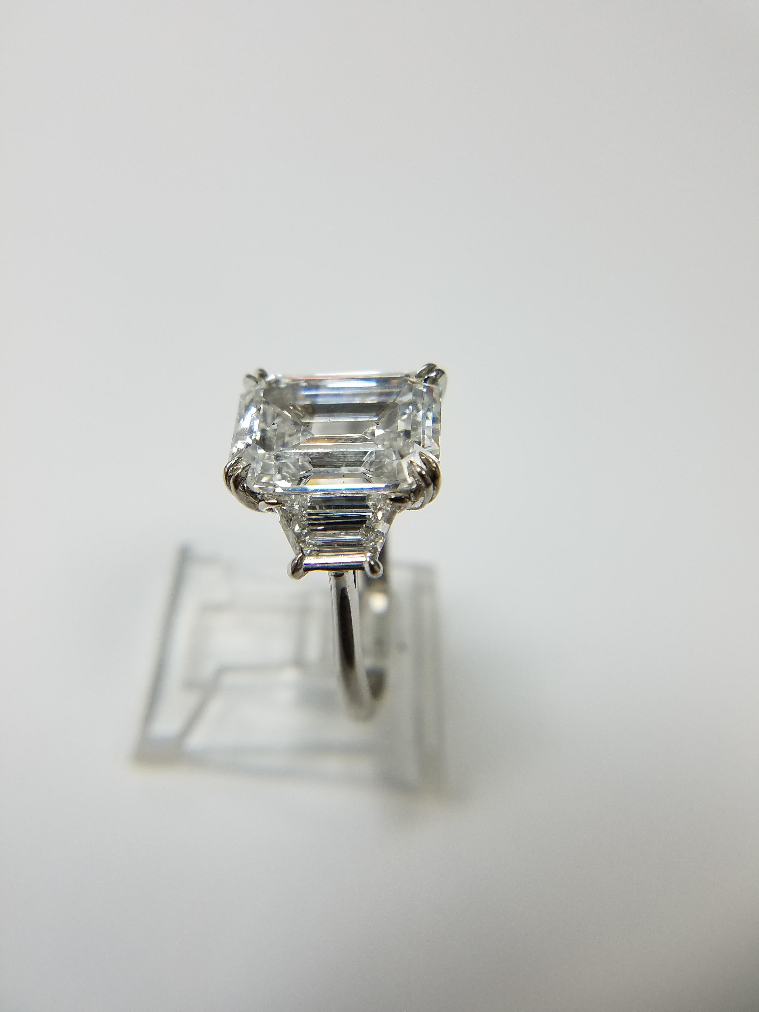 GIA Certified 6.55 carat Emerald Cut Diamond with a D color and SI1 clarity set in a Platinum Ring with 2 trapezoid shaped diamonds weight 0.51 carats each and a unique double prong that ensures the diamond is safe while adding a unique style. 
GIA