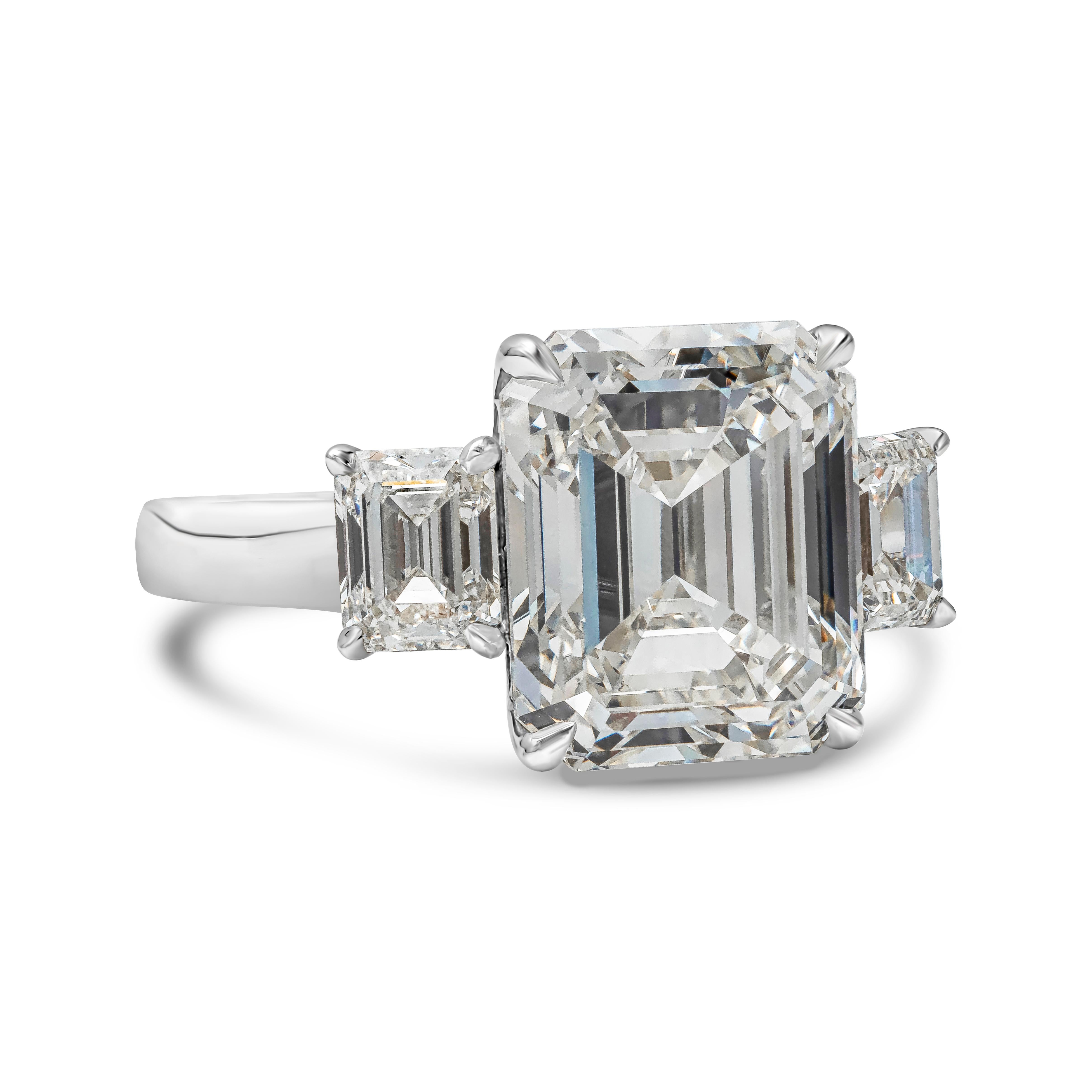 An elegant three-stone engagement ring, showcasing a 6.73 carats emerald cut diamond certified by GIA as J color and VS2 clarity. Flanked by smaller emerald cut diamonds weighing 1.22 carats total. Each stone is set on a four prong setting. Finely