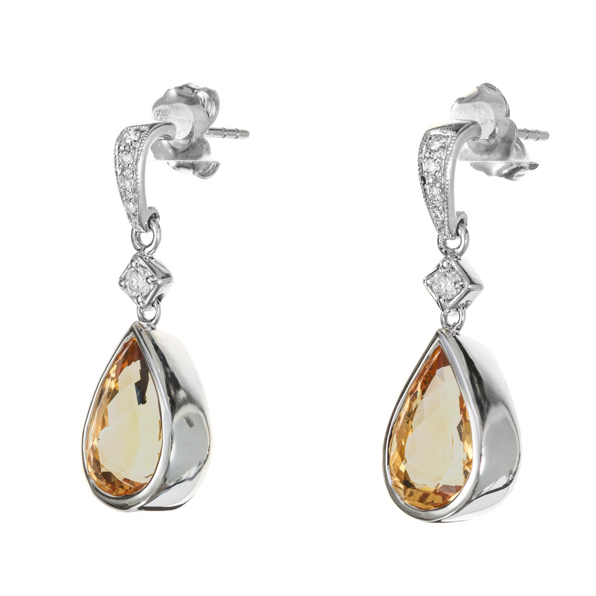 Yellow topaz and diamond dangle earrings. Two 5.78ct precious orange yellow pear shaped bezel topaz dangle earrings, each with 5 round cut brilliant cut diamonds in 14k white gold.

2 pear shape orange yellow topaz, approx.. 5.78cts GIA Certificate