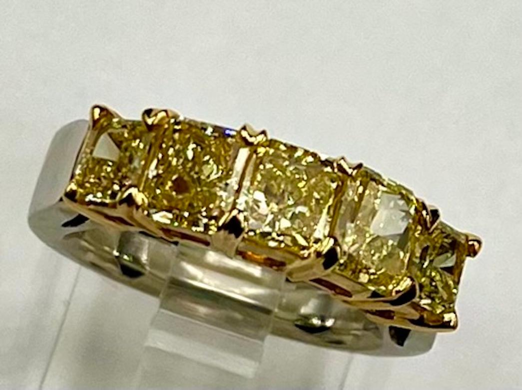 This is a classic 5 stone band set with a 3/4 Carat center Cut Cornered Rectangular Modified Brilliant Diamond graded by GIA as being Fancy Intense Yellow in color and a VS1 in clarity. The 2 diamonds immediately next to the center are also 3/4