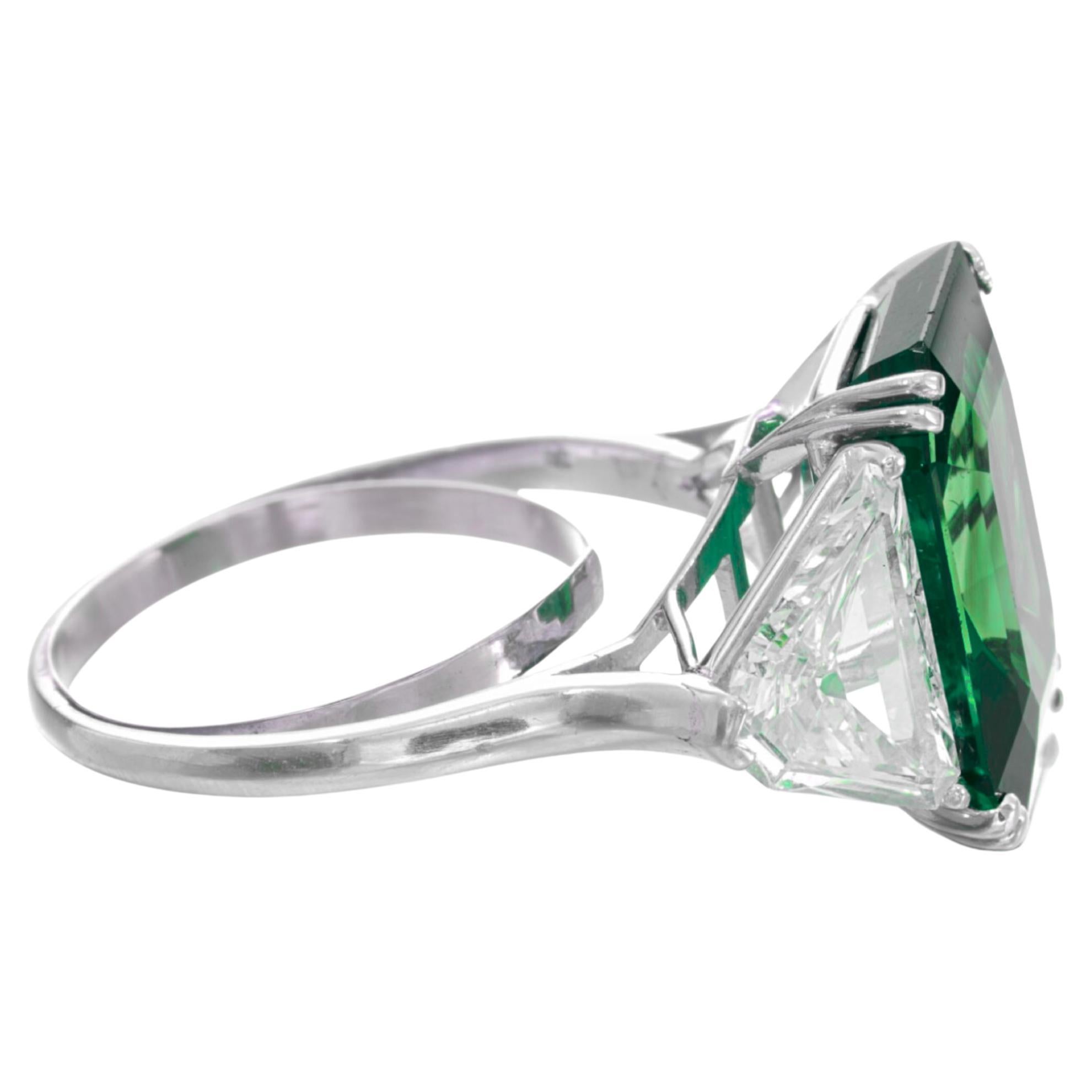 An exquisite intense green, certified by GIA. With a total carat weight of 7.63 carats, the emerald is beautifully cut in a pear shape, showcasing its captivating vivid green color. Surrounding the emerald are natural trillion side diamonds totaling