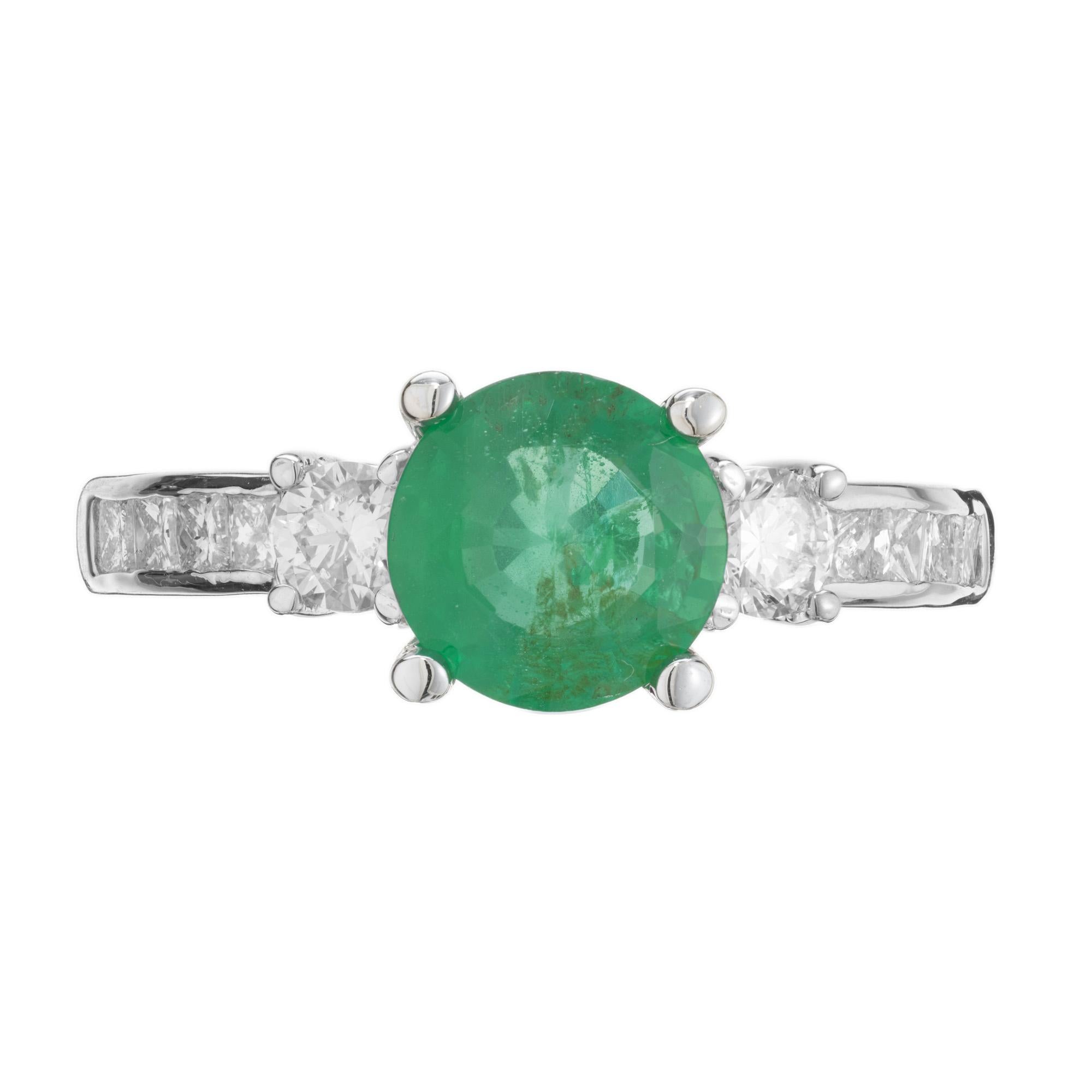 Emerald and diamond three-stone engagement ring. GIA certified natural round emerald center stone, mounted in a 14k white gold setting with two round brilliant cut side diamonds, accented with 8 princess cut diamonds, 4 on each side, along the