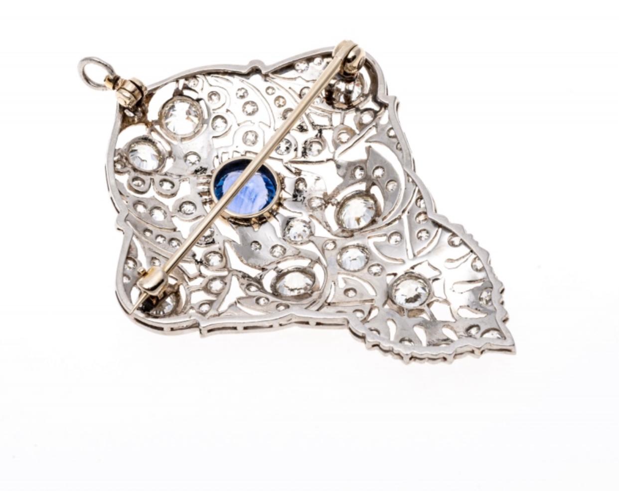 This amazing antique Edwardian era brooch (and pendant) contains a center round faceted, cornflower blue color natural sapphire from Sri Lanka, approximately 0.94 CTS and bezel set. Surrounding the sapphire are scrolls of openwork filigree, milgrain