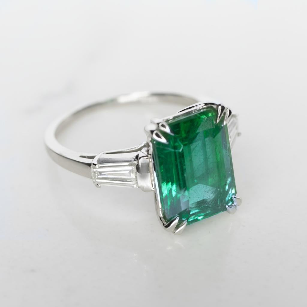 Este impresionante anillo de platino exhibe una esmeralda natural de color verde vivo, certificada por el GIA (Informe n.º 2231454309). La gema exhibe una transparencia excepcional y un color verde rico y saturado, bellamente complementado por dos